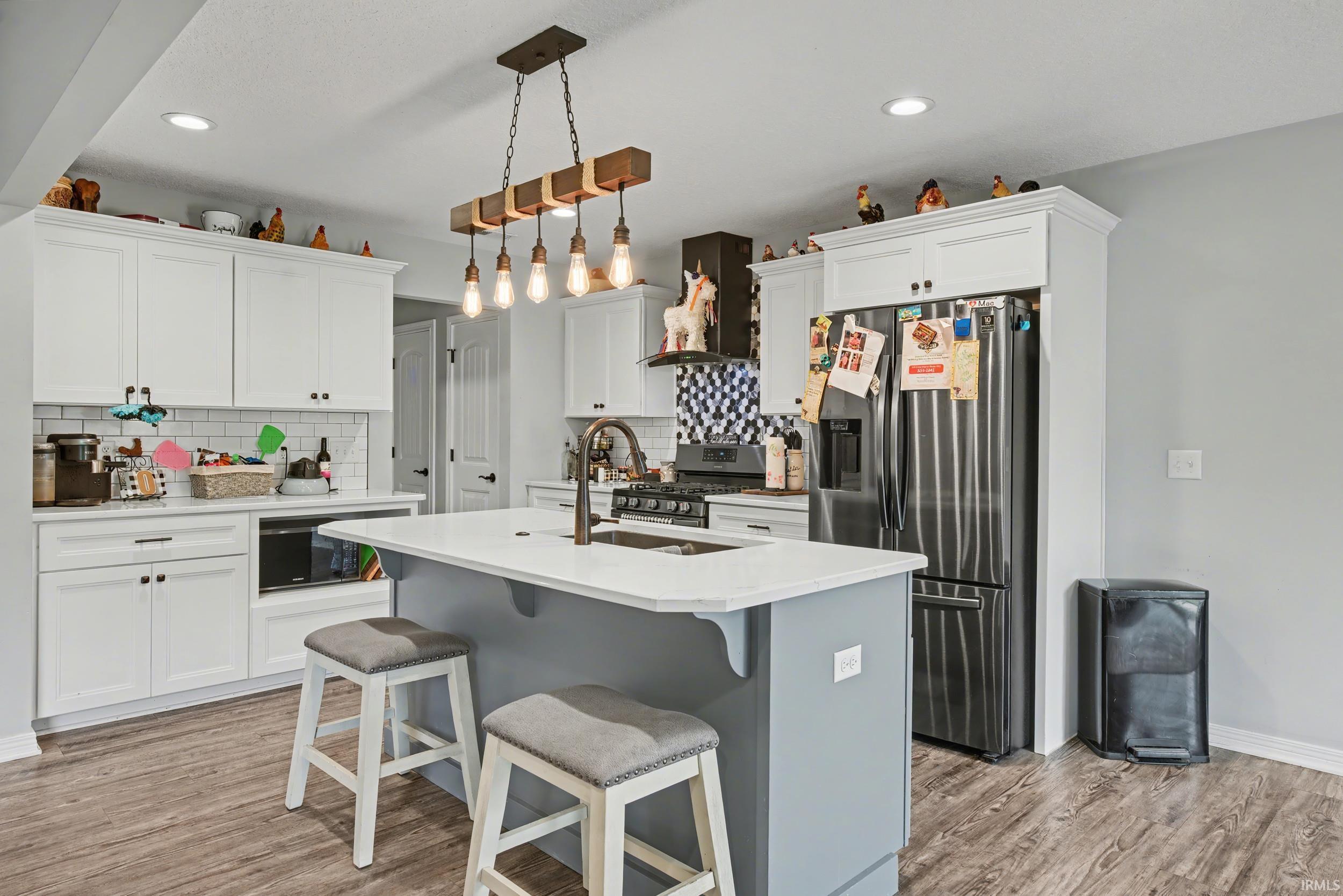 Kitchen featuring white shaker-style cabinetry, a contrasting gray island with a white countertop, stainless steel appliances, wood-finish flooring, and a white subway tile backsplash