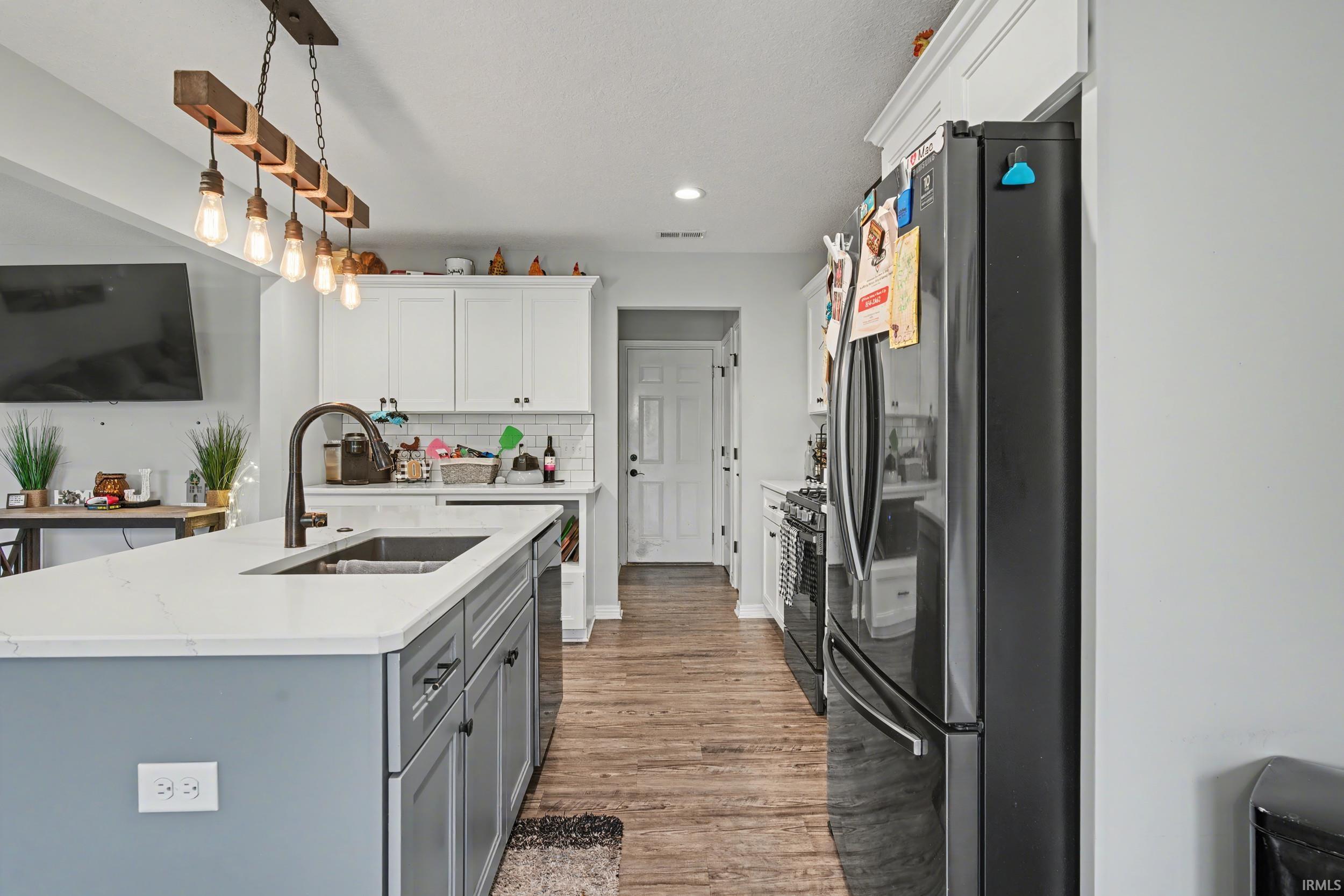 Kitchen featuring a large island with an undermount sink, quartz countertops, wood-finish flooring, white upper cabinetry, and a black appliance package