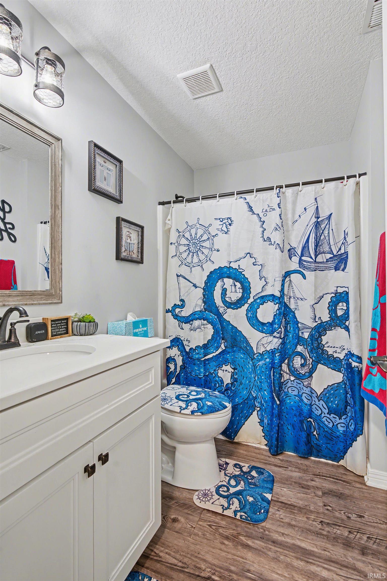 Bathroom featuring a white vanity with an integrated sink, wood-finish flooring, and a shower/tub combination