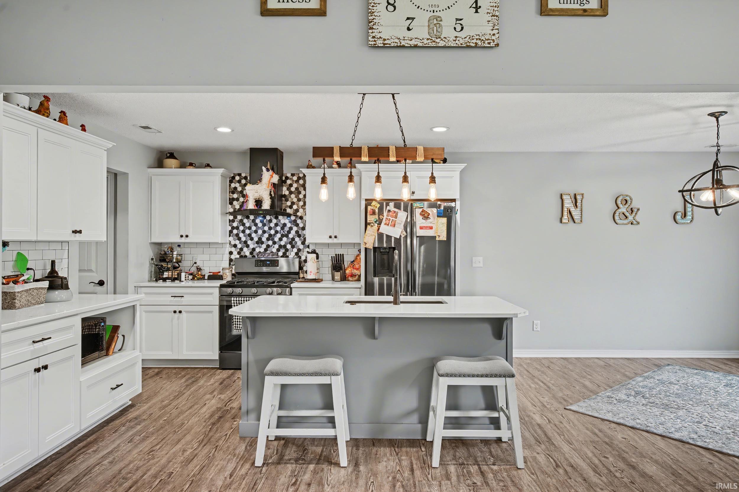 Kitchen featuring a central island with countertop seating, stainless steel appliances, white cabinetry, wood-finish flooring, and a decorative tile backsplash