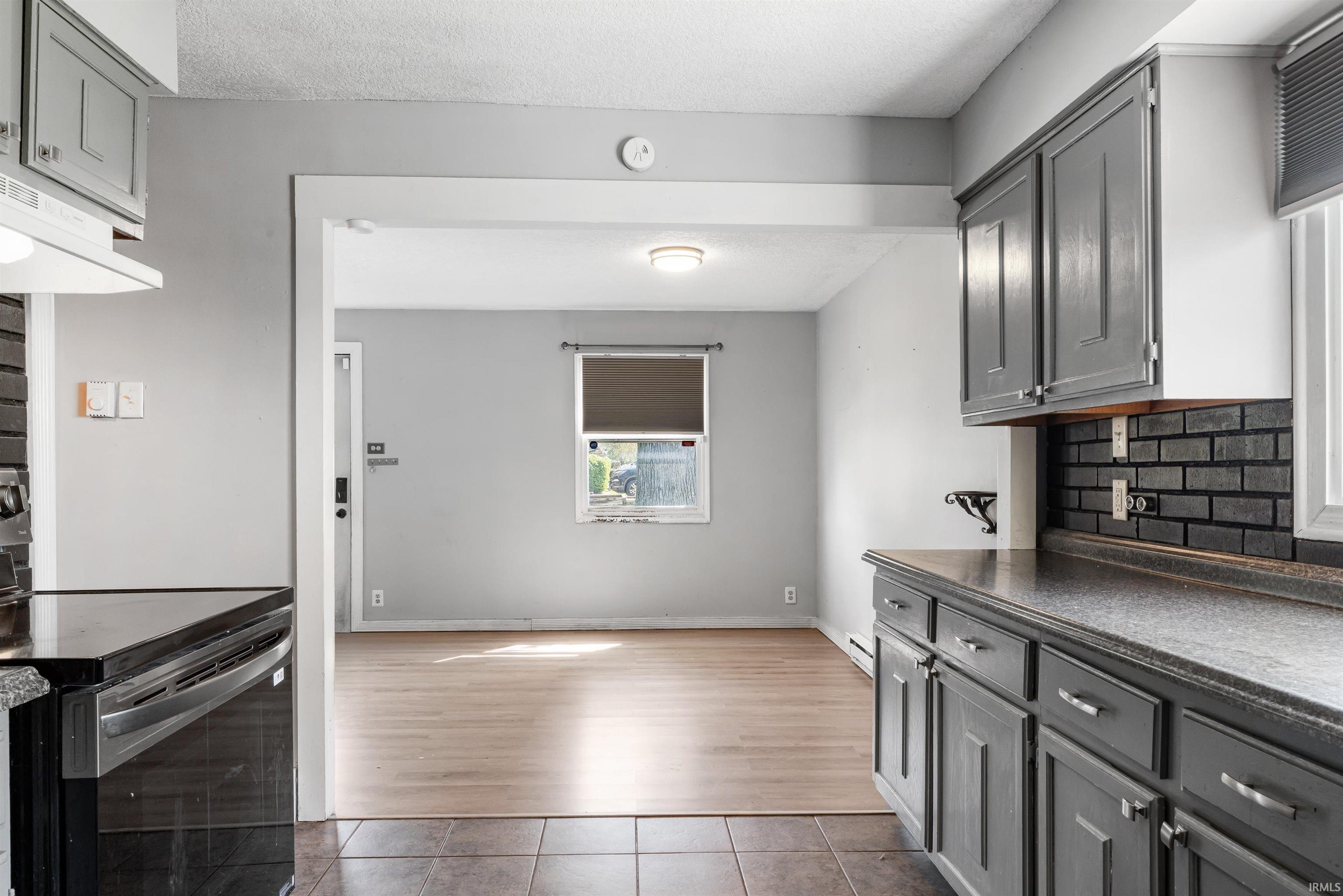 Kitchen featuring gray cabinetry with brushed nickel hardware, a black subway tile backsplash, and dark countertops