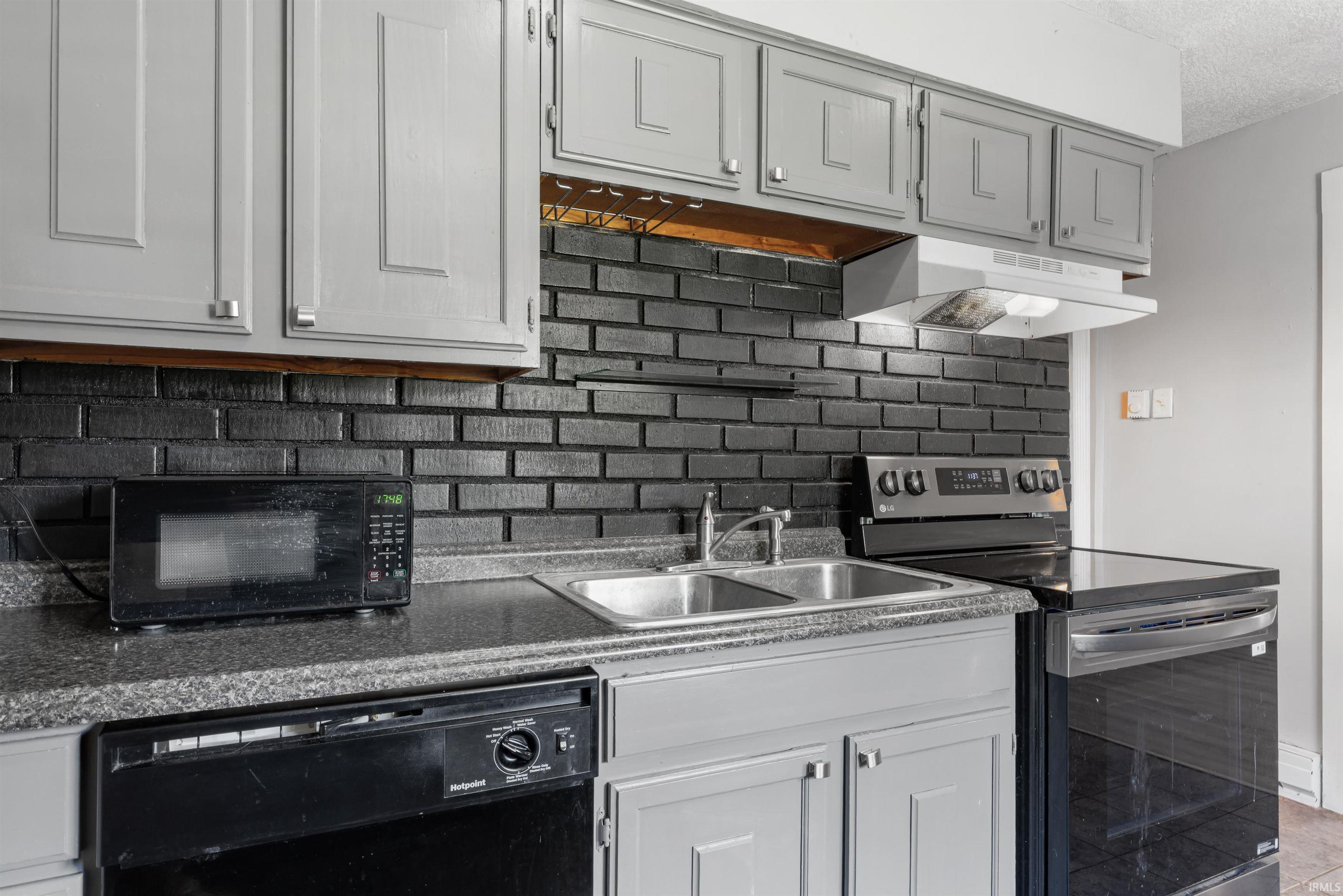 Kitchen featuring gray cabinetry with silver hardware, a black brick-style backsplash, and dark speckled countertops