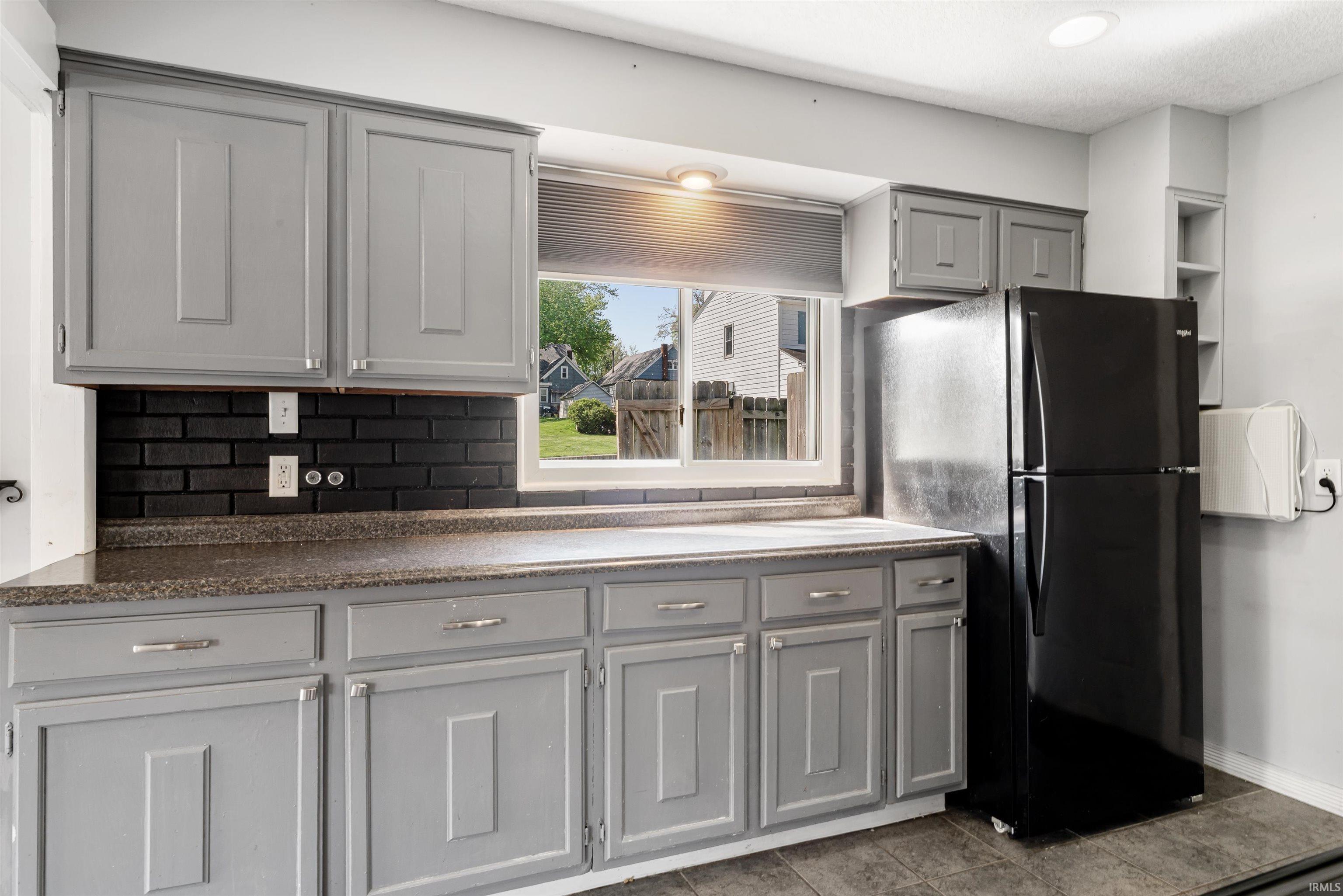 Kitchen featuring gray shaker-style cabinetry with chrome hardware, a black brick-patterned backsplash, and a dark speckled countertop