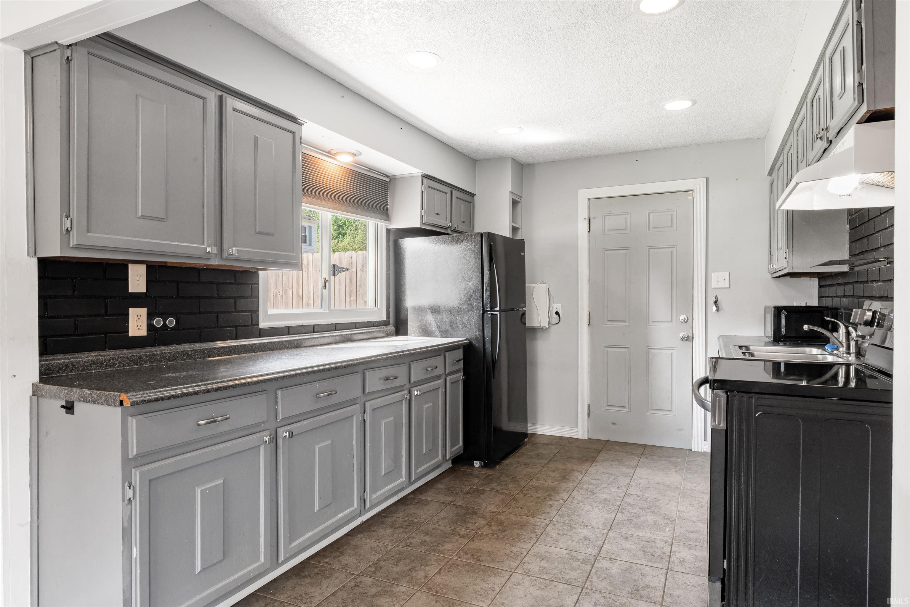 Kitchen featuring gray cabinetry, black subway tile backsplash, and dark countertops