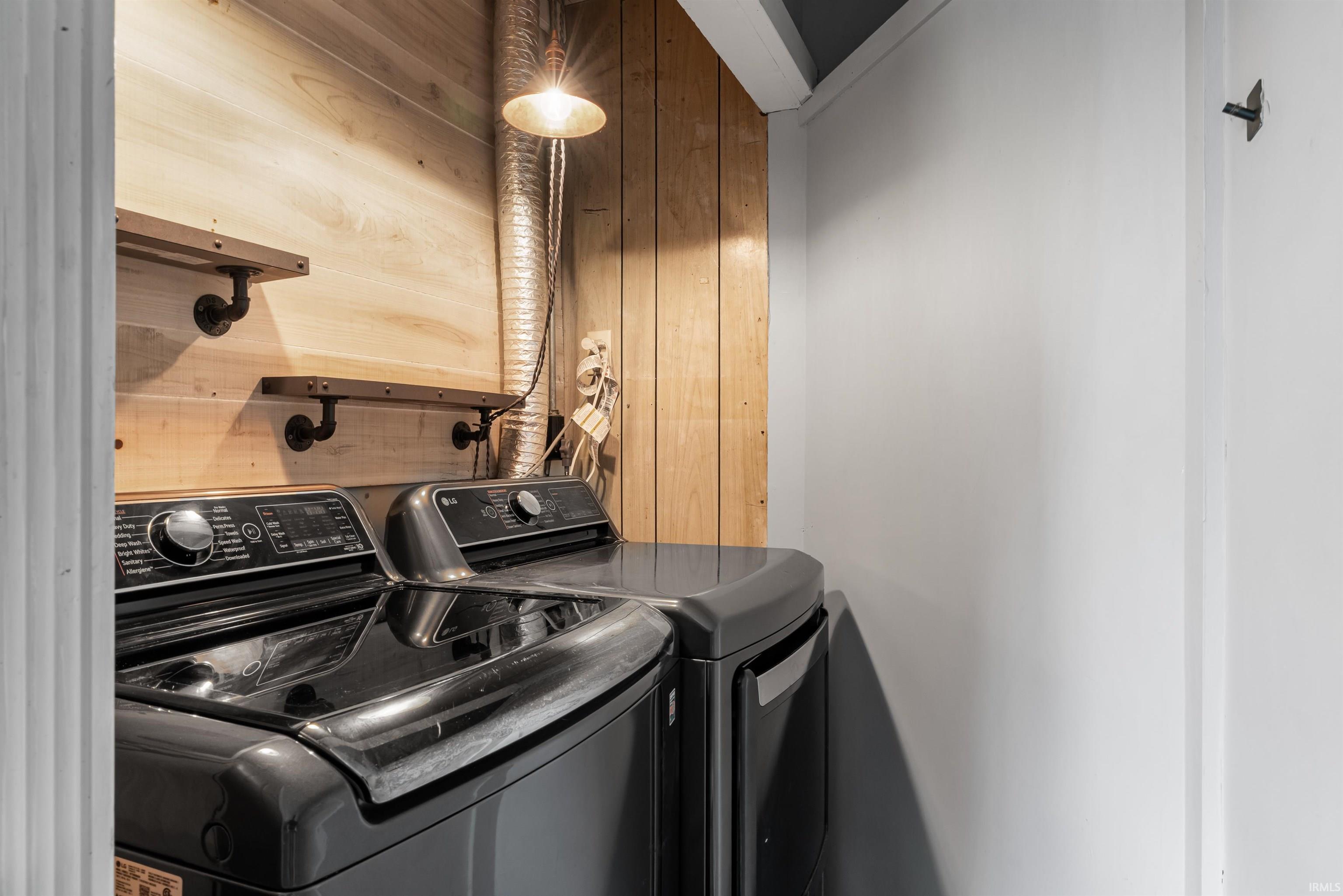 Dedicated laundry area featuring a wood-paneled wall, two wall-mounted shelves with dark industrial-style brackets, and a wall-mounted light fixture