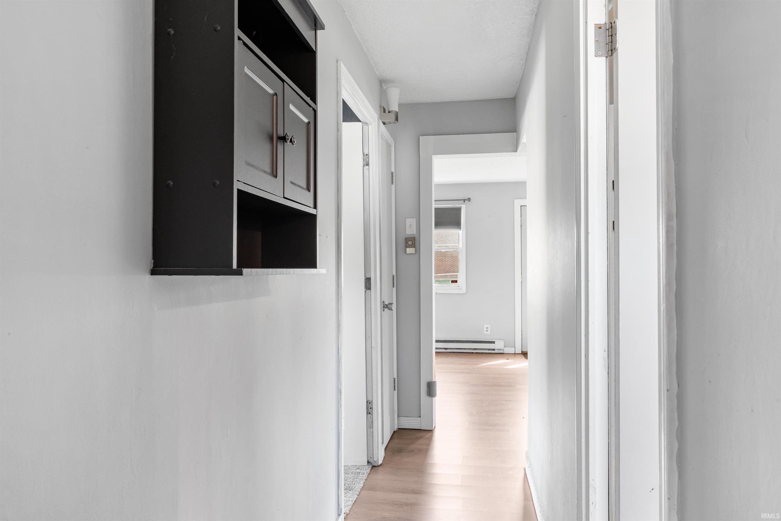 Hallway featuring wood-finish flooring, light grey wall paint, and a wall-mounted dark wood cabinet with double doors and open shelving