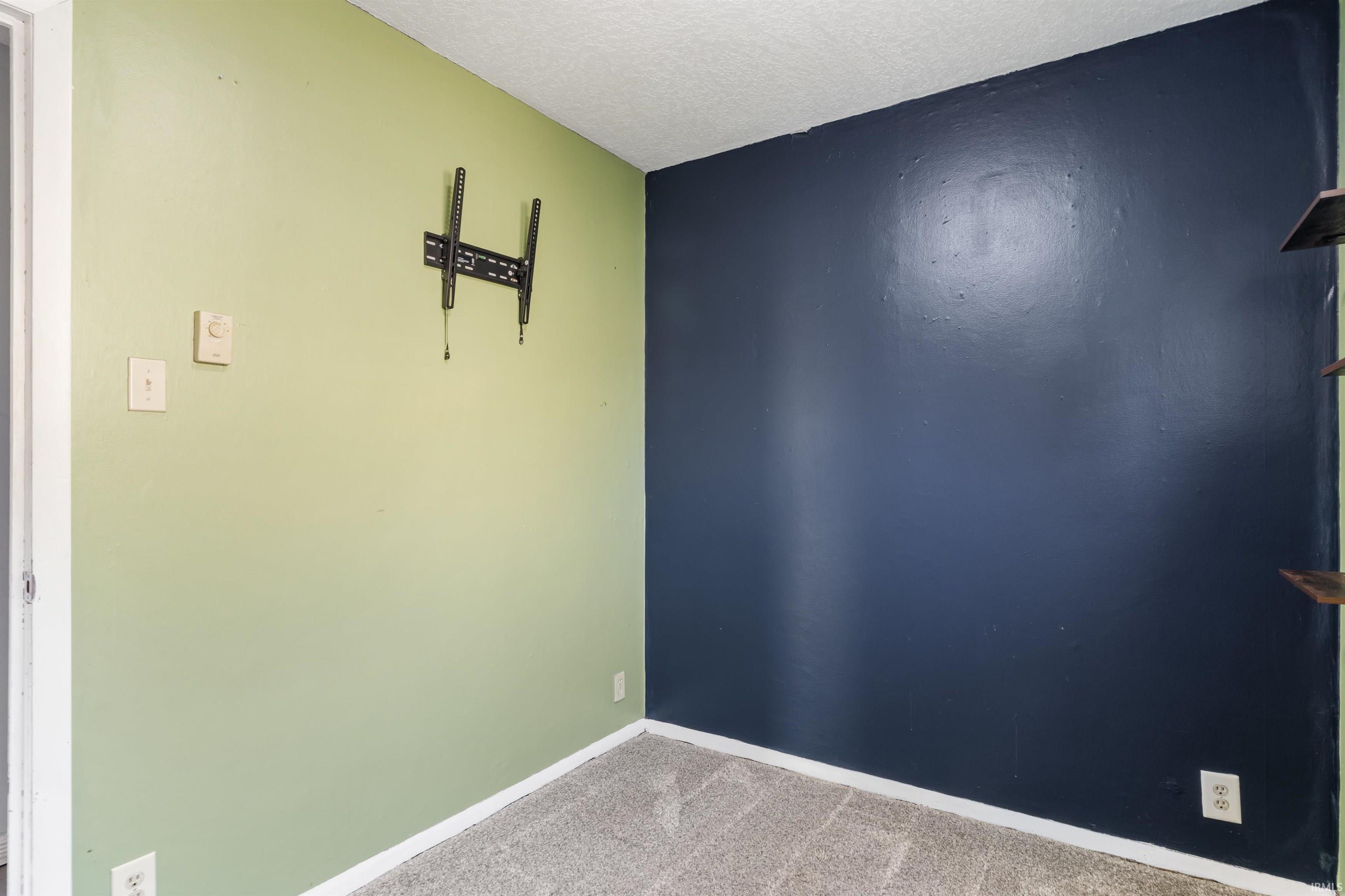 Interior space featuring light green and dark blue accent walls, gray carpet flooring, and white baseboards