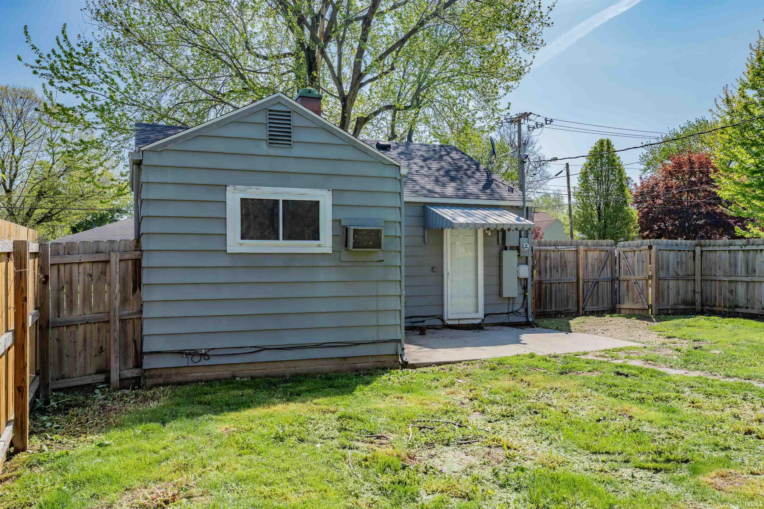Expansive backyard with a wood privacy fence, concrete patio, and mature trees