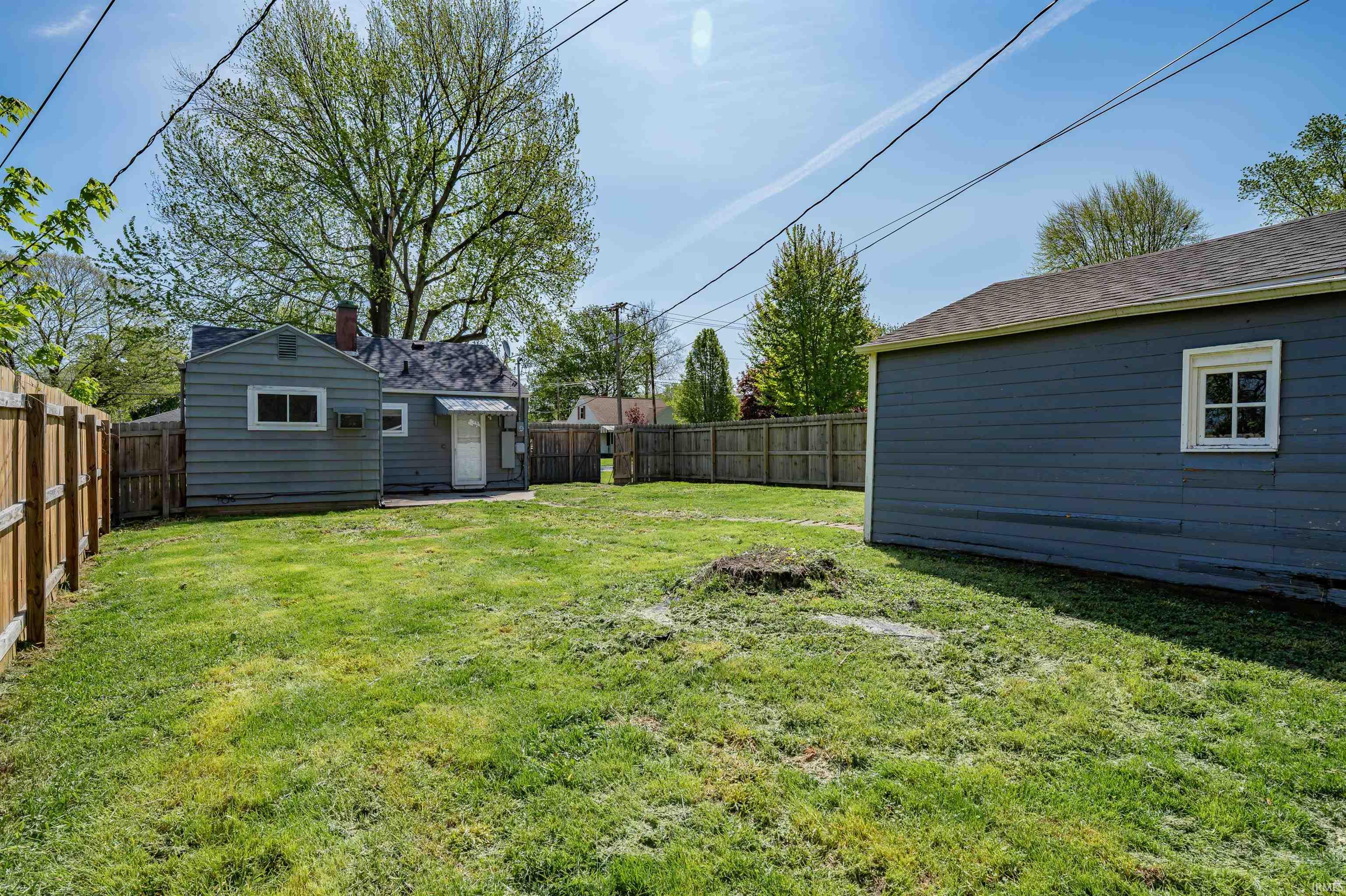 Expansive green lawn featuring a detached auxiliary building with white trim, a separate garage structure with a multi-pane window, and a full perimeter wood fence