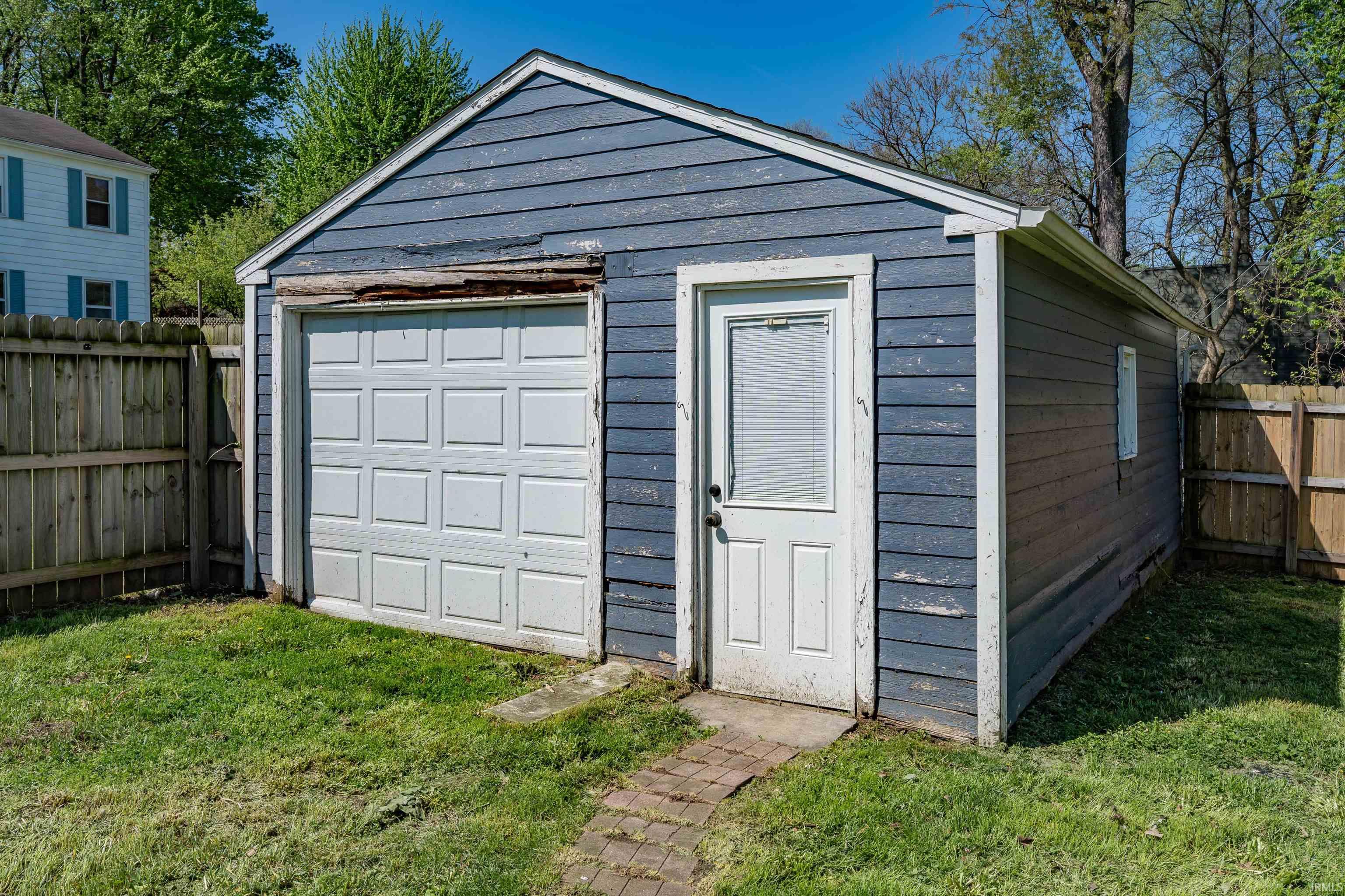 Detached garage with blue siding, white overhead door, and a separate service door with privacy screen