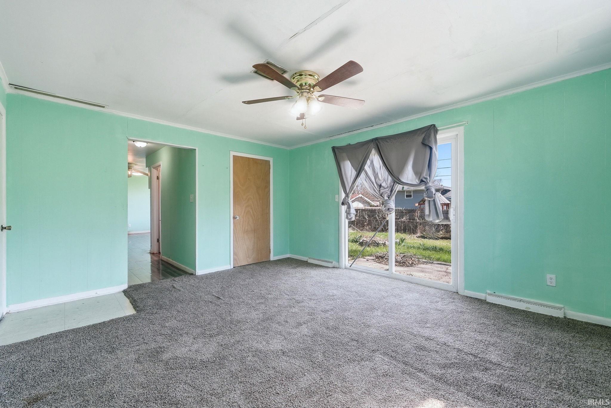Spacious room featuring light green walls, a ceiling fan with integrated lighting, and gray carpeting