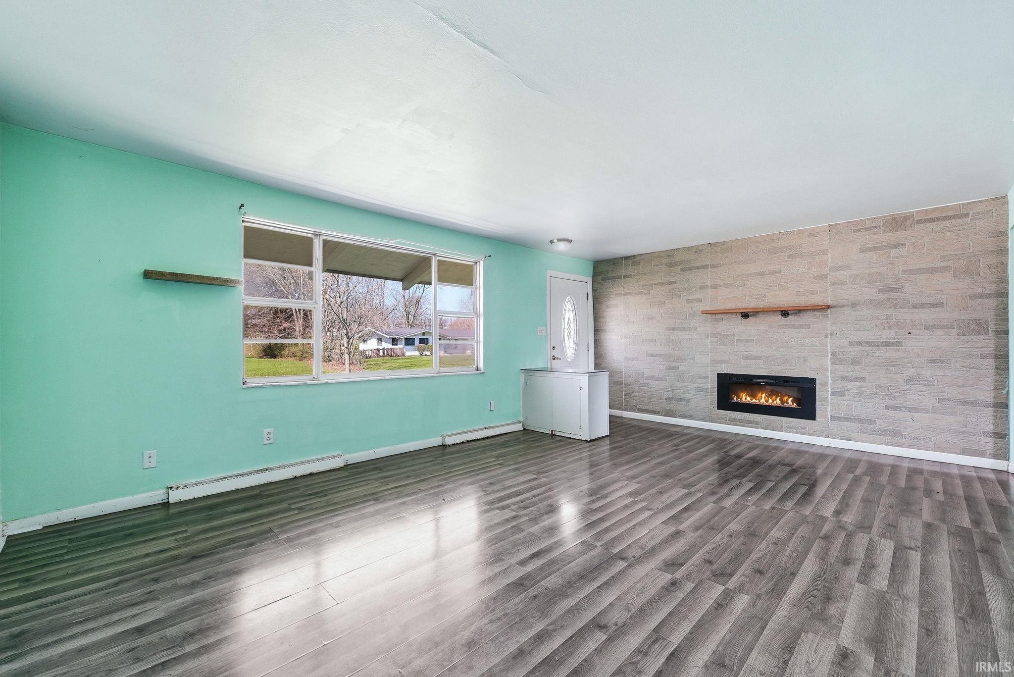 Spacious room featuring wood-finish flooring, a wall-mounted electric fireplace with a wood mantle, and a large window