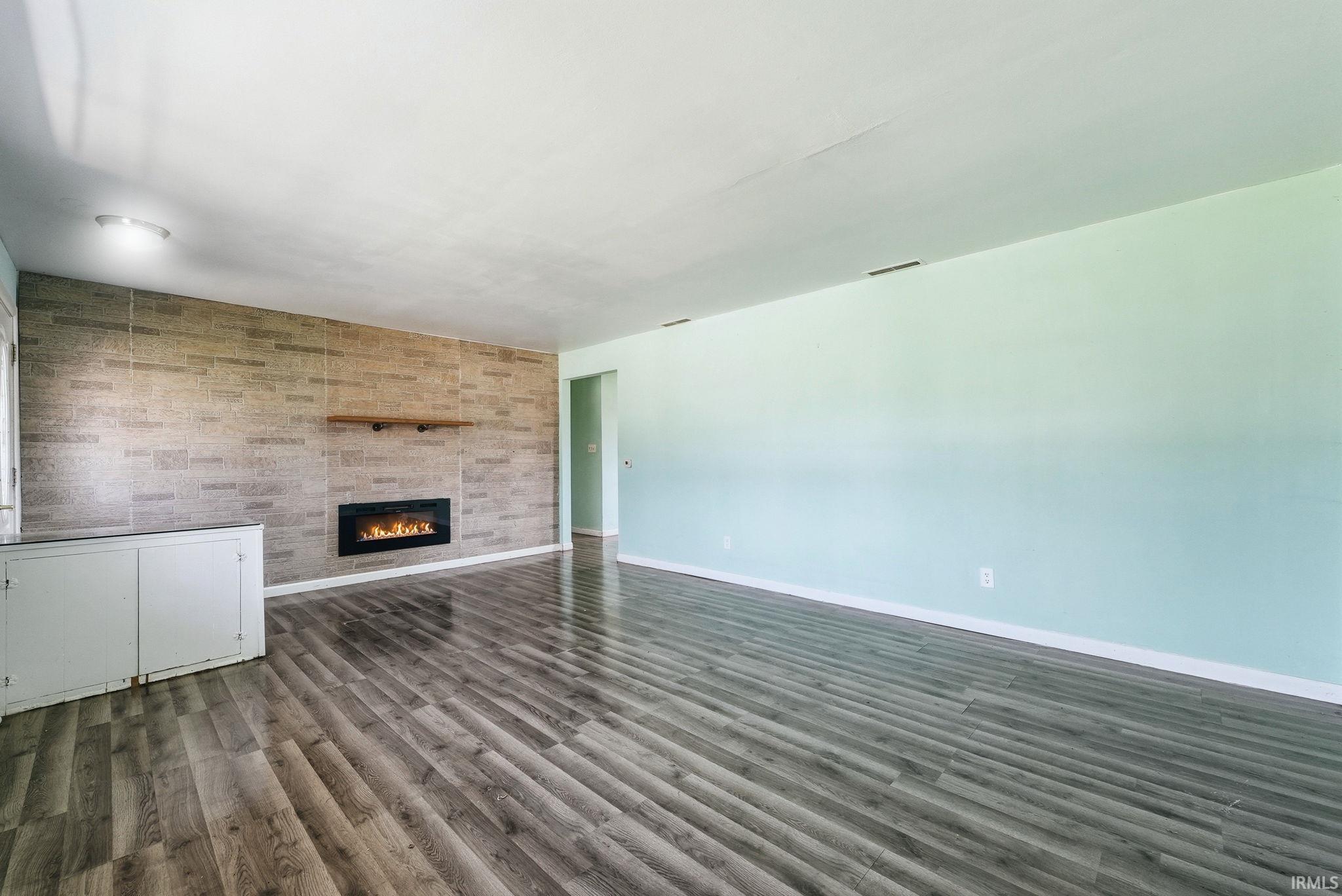 Spacious room featuring wood-finish flooring, a wall-mounted fireplace with a stone-finish surround, a wooden mantel, and built-in cabinetry