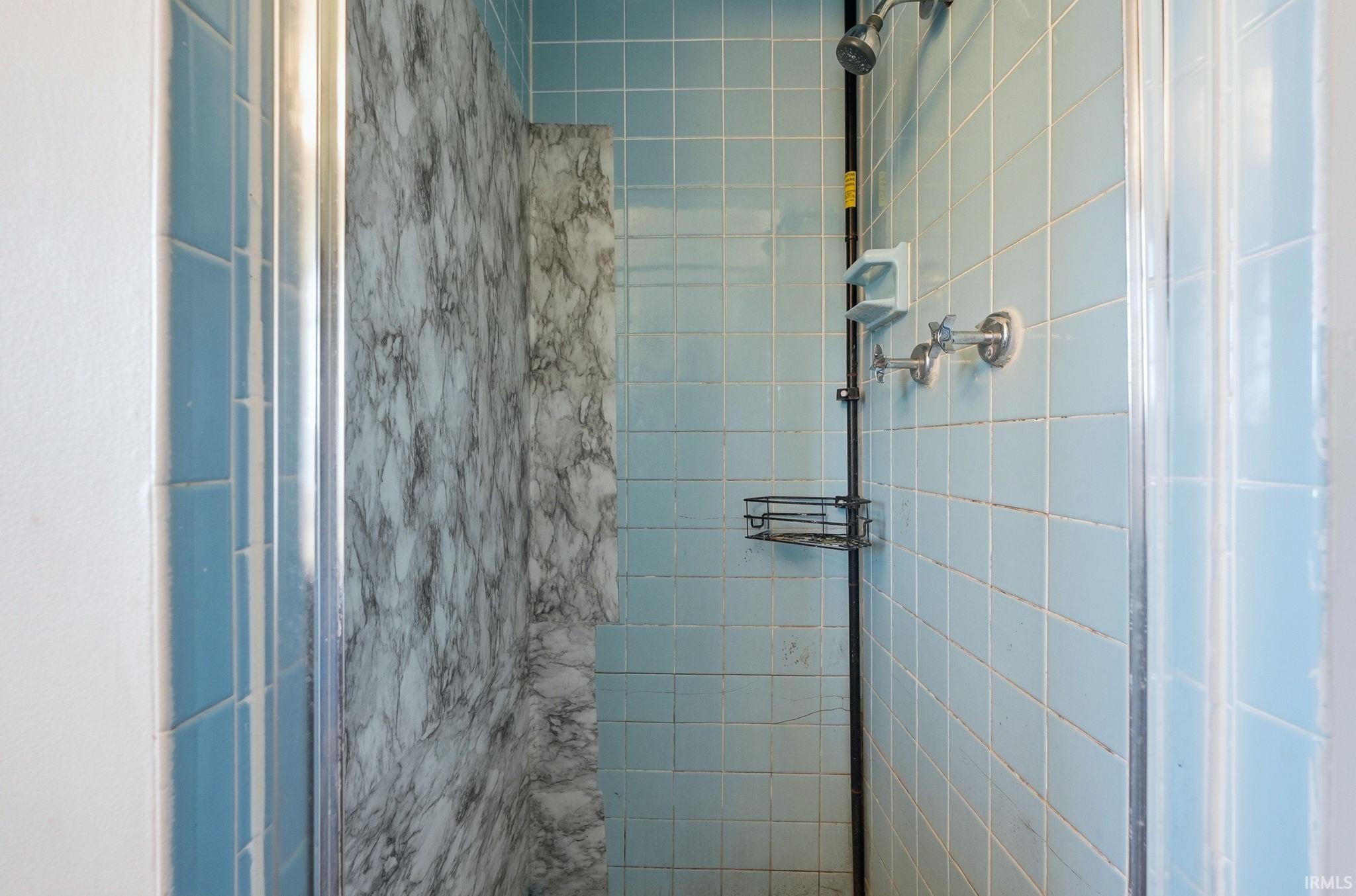 Shower enclosure featuring light blue tile walls and a contrasting marble-patterned panel