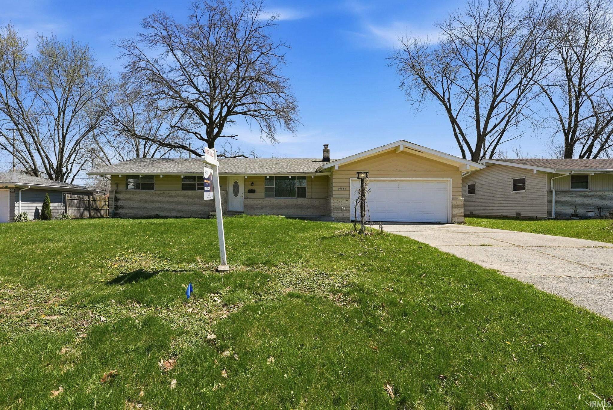 Ranch-style residence featuring a yellow siding exterior, a white front door, and a single-car garage with an overhead door