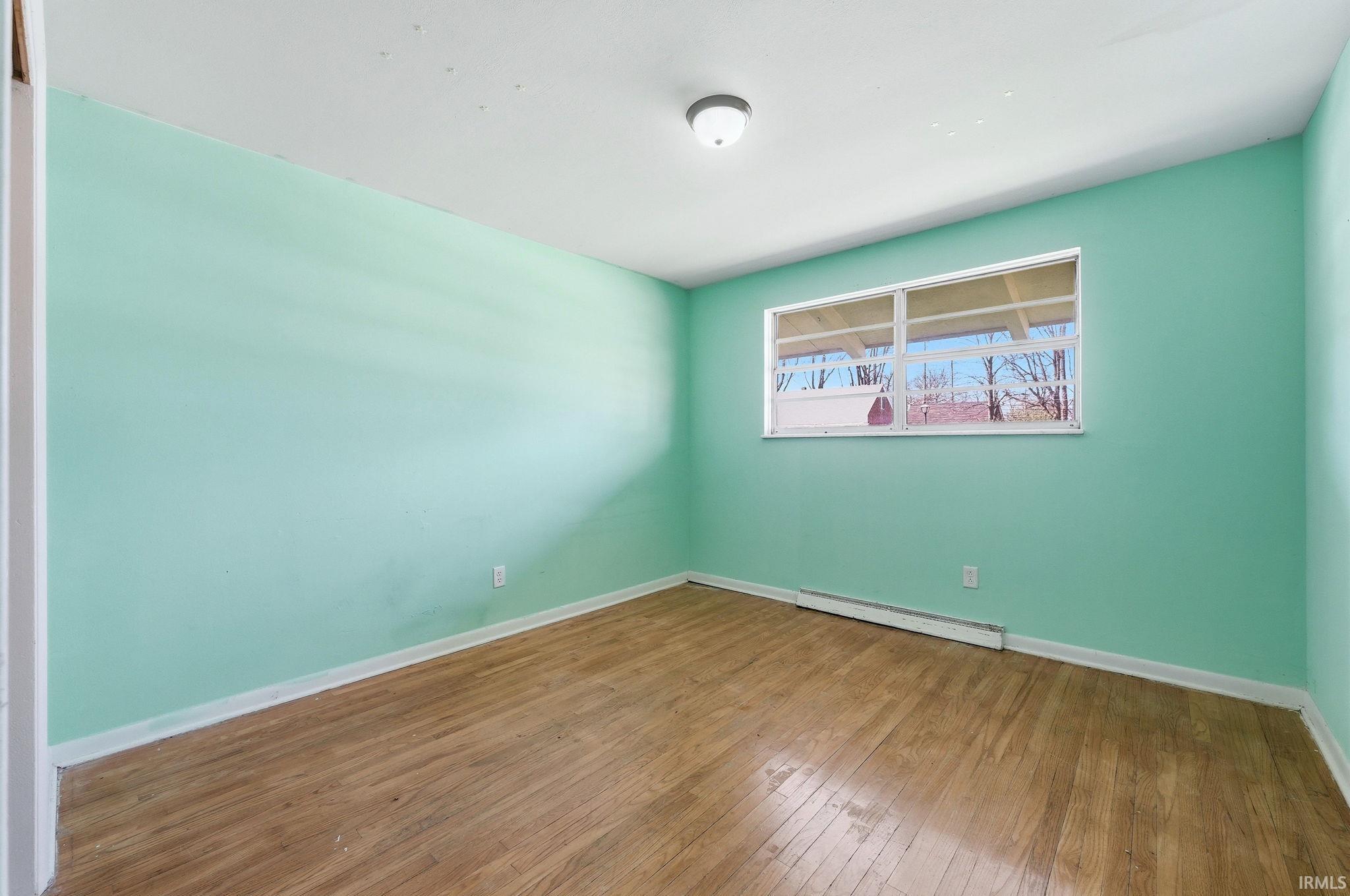 Spacious interior room featuring wood-finish flooring, light teal wall paint, and white trim