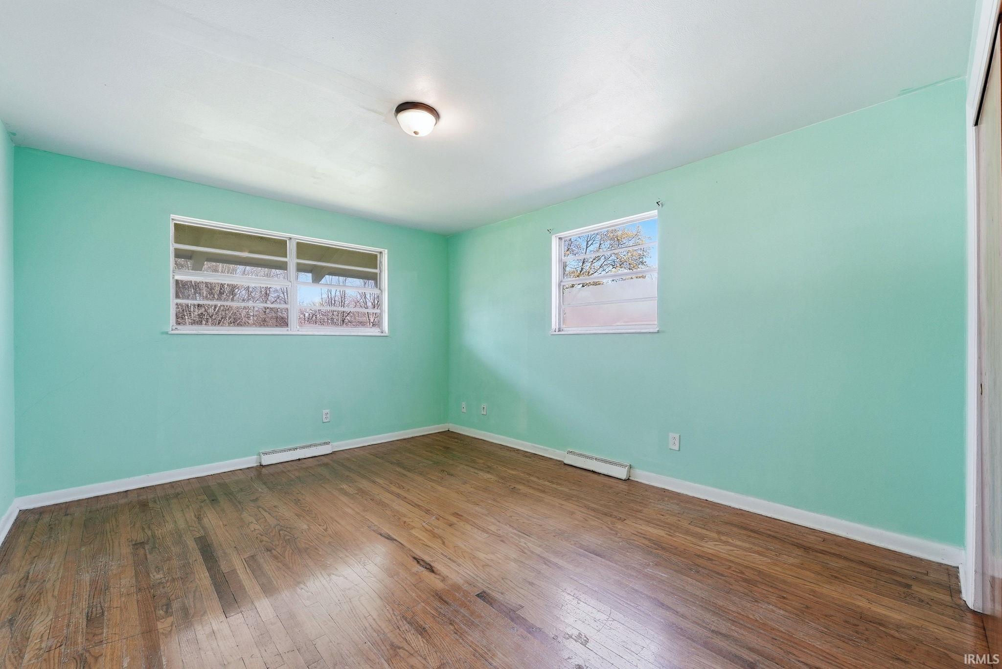 Spacious interior room featuring wood-finish flooring, light aqua walls, and white trim