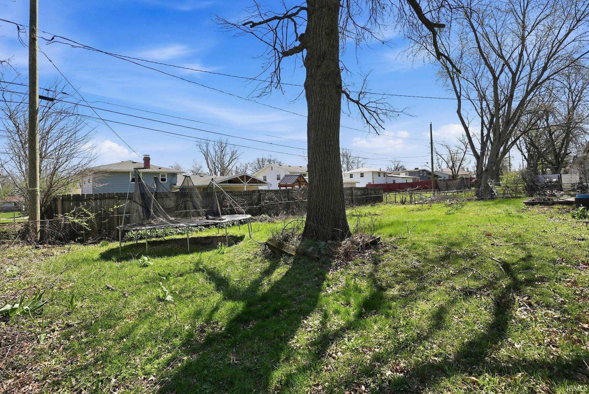 Expansive green space featuring a large mature tree, partial wood fencing, and a utility pole