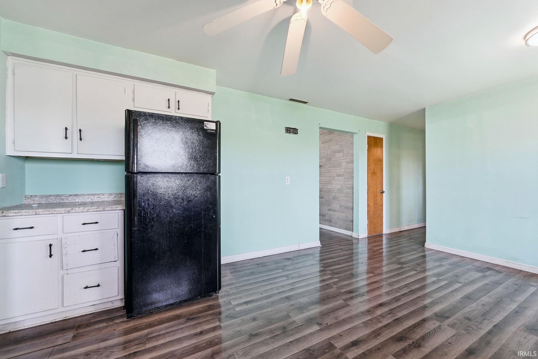 Open-concept living area featuring wood-finish flooring, white cabinetry with dark hardware, and a ceiling fan with integrated lighting