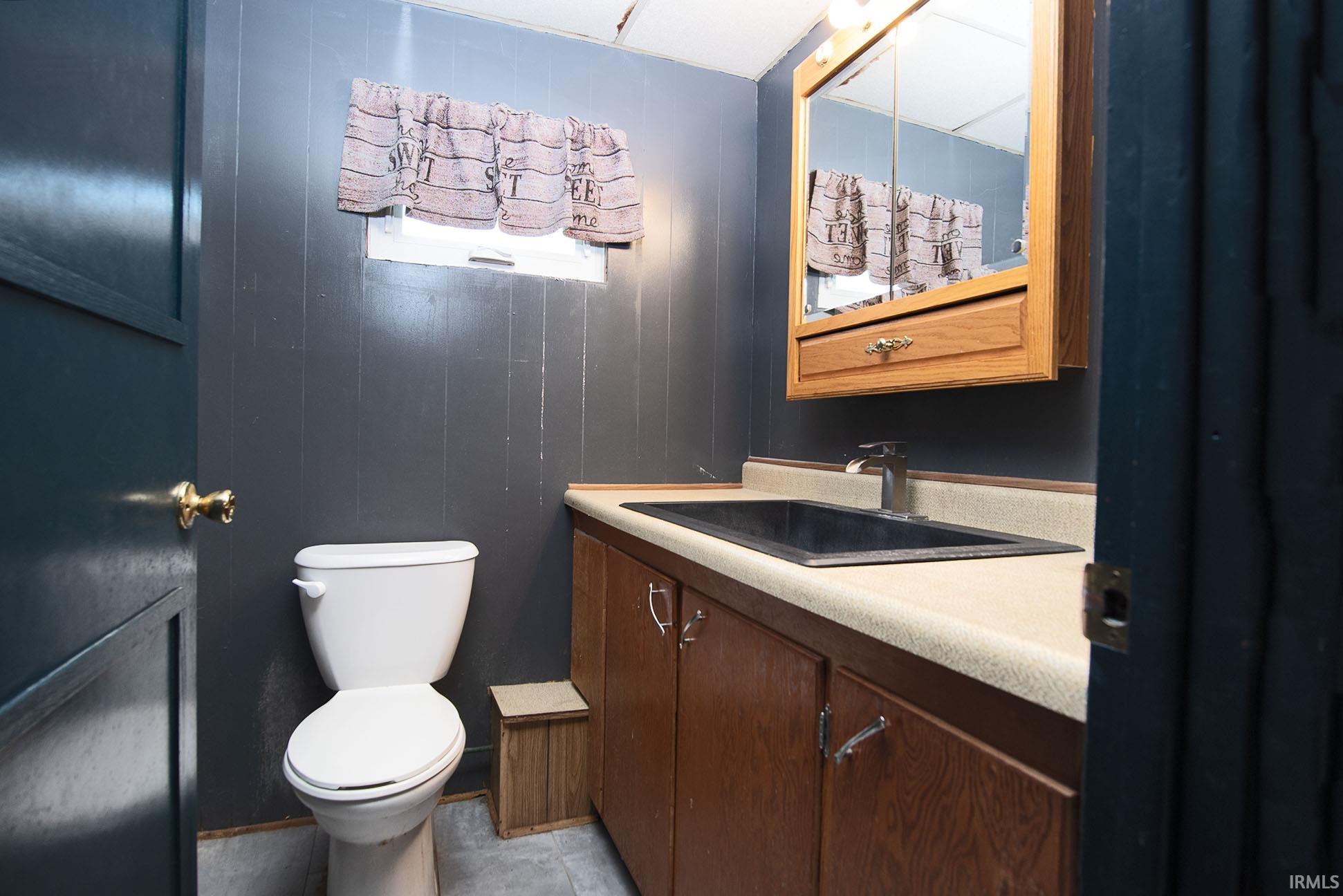 Bathroom with dark gray paneling, a white toilet, and a light-colored vanity countertop