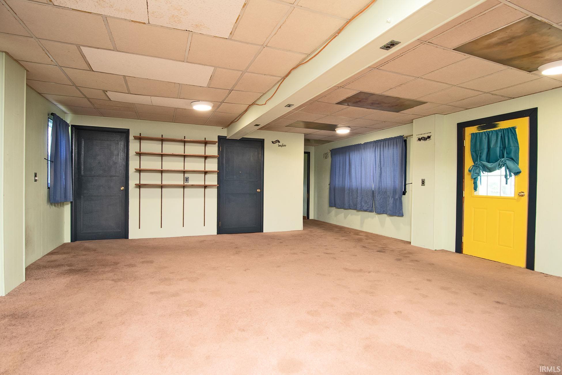 Spacious carpeted room with light-toned walls, built-in shelving, multiple entryways, and overhead lighting