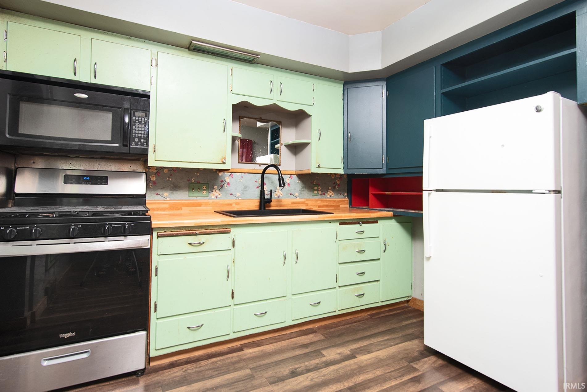 Kitchen featuring wood-finish flooring, light green cabinetry, butcher block style countertops, and a black sink with a matte black faucet