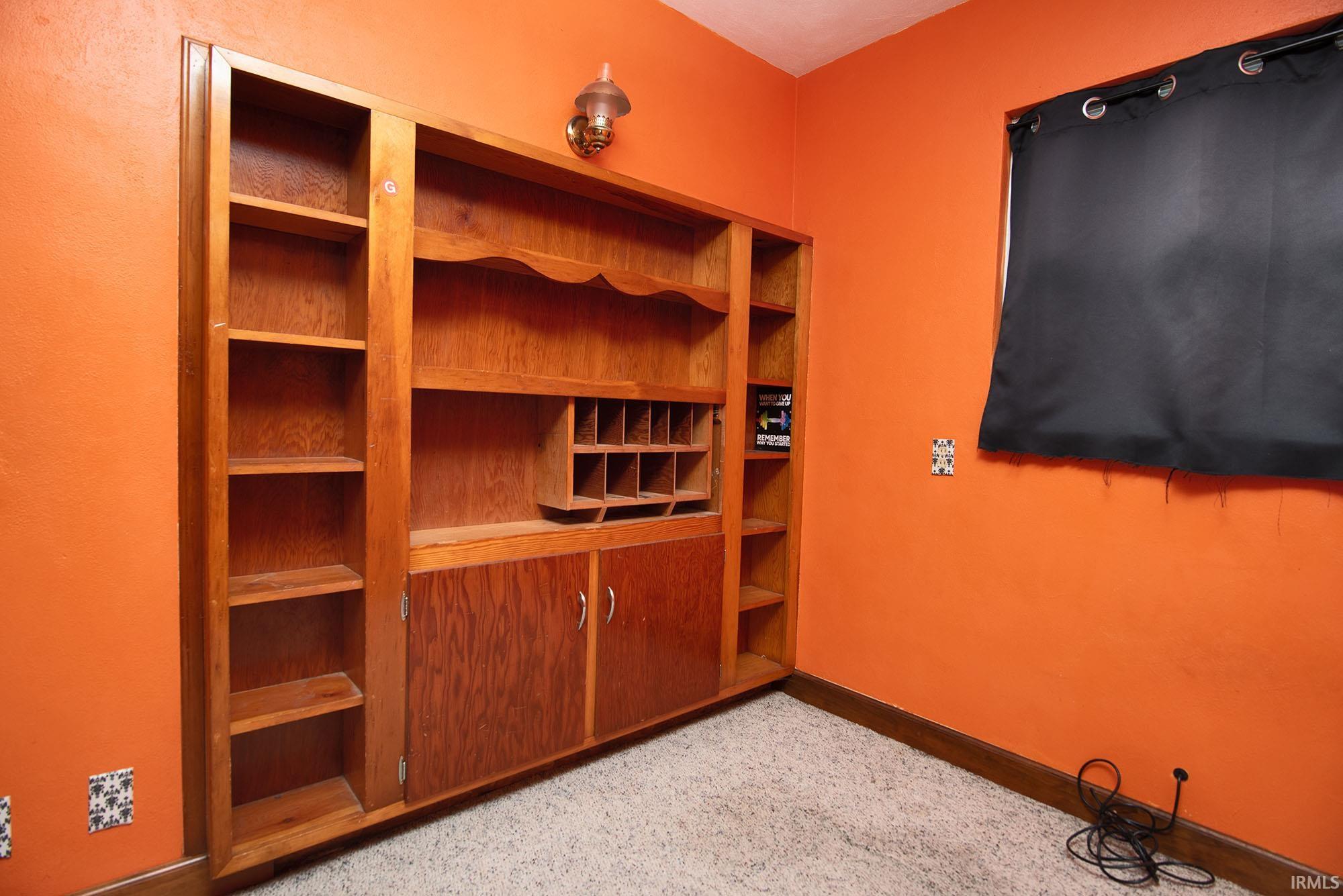 Custom built-in wood-finish shelving unit with integrated cabinets and a desk organizer, complemented by a wall-mounted glass sconce and a window with a black blackout curtain