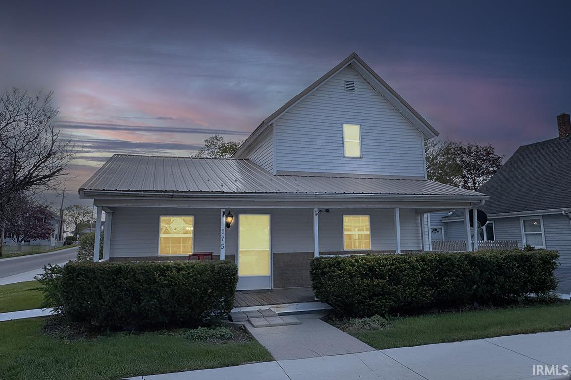 Two-story residence featuring light-colored siding, a covered front porch with white columns, and a metal roof