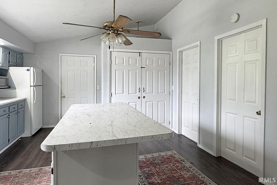Central kitchen island with a light-toned countertop, dark wood-finish flooring, and white paneled doors