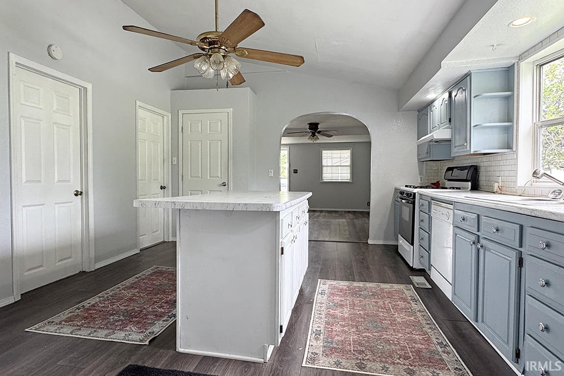 Kitchen featuring a central island with a solid surface countertop, wood-finish flooring, light blue cabinetry with clear glass knobs, subway tile backsplash, and a vaulted ceiling with a ceiling fan