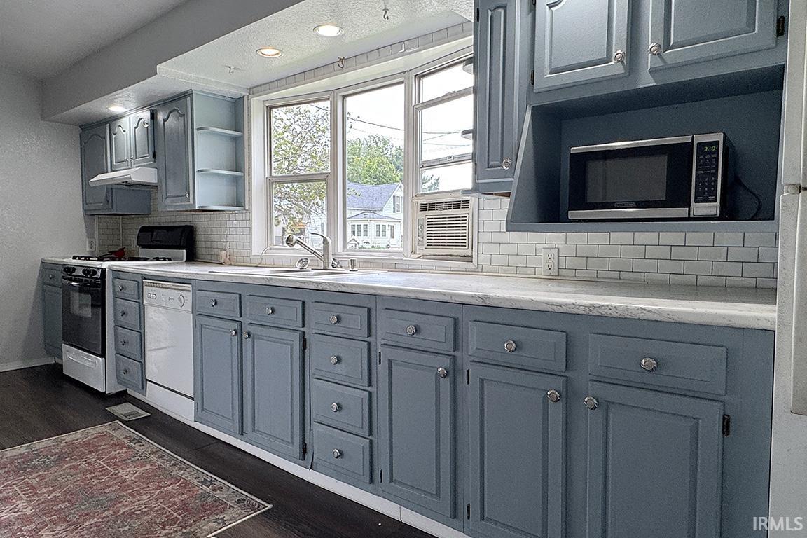 Kitchen featuring custom blue cabinetry, white subway tile backsplash, light-toned countertops, a stainless steel sink with a chrome faucet, and recessed lighting