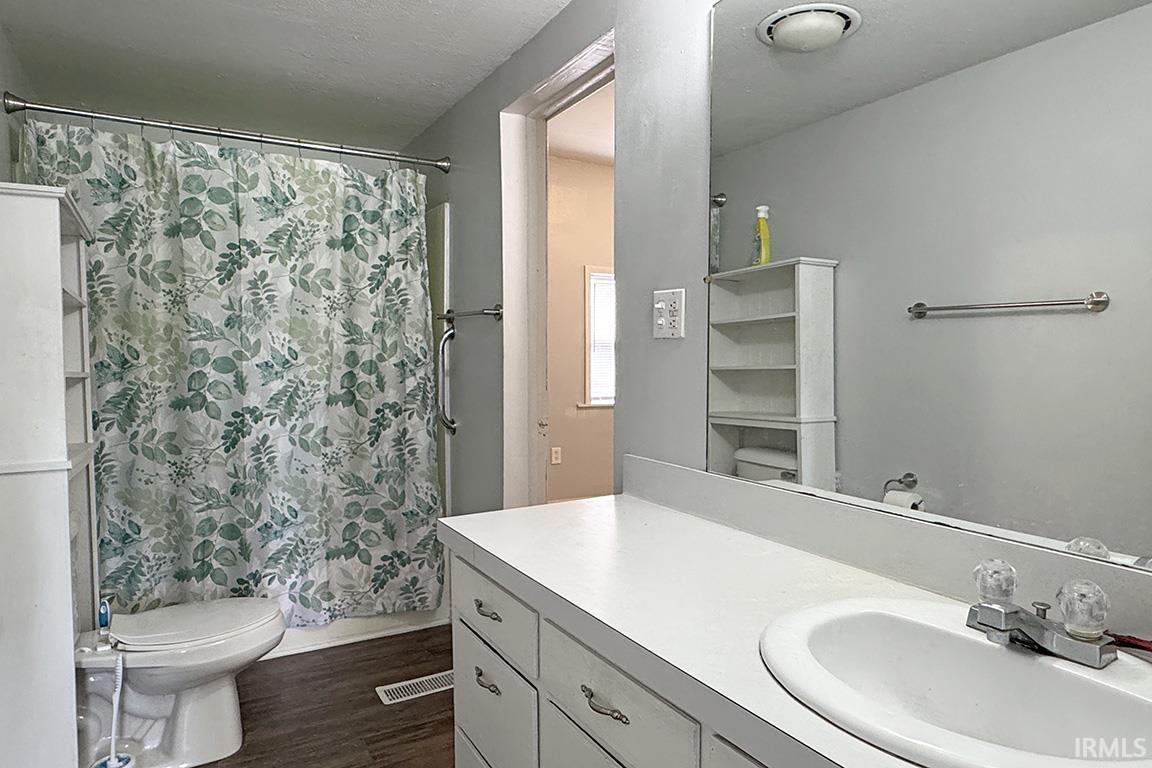 Bathroom featuring a white vanity with integrated sink, a large wall-mounted mirror, and wood-finish flooring