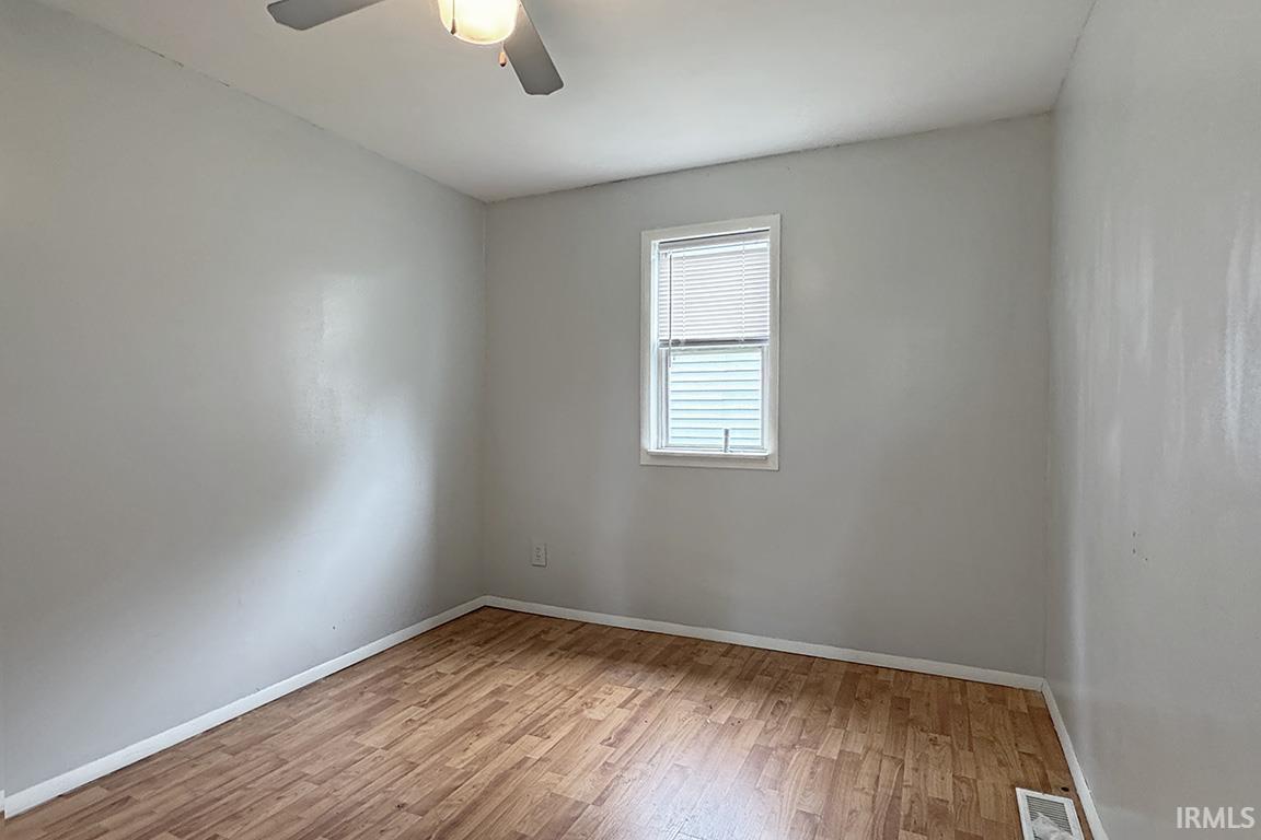 Neutral gray walls featuring wood-finish flooring, a ceiling fan with integrated lighting, and a single window with blinds