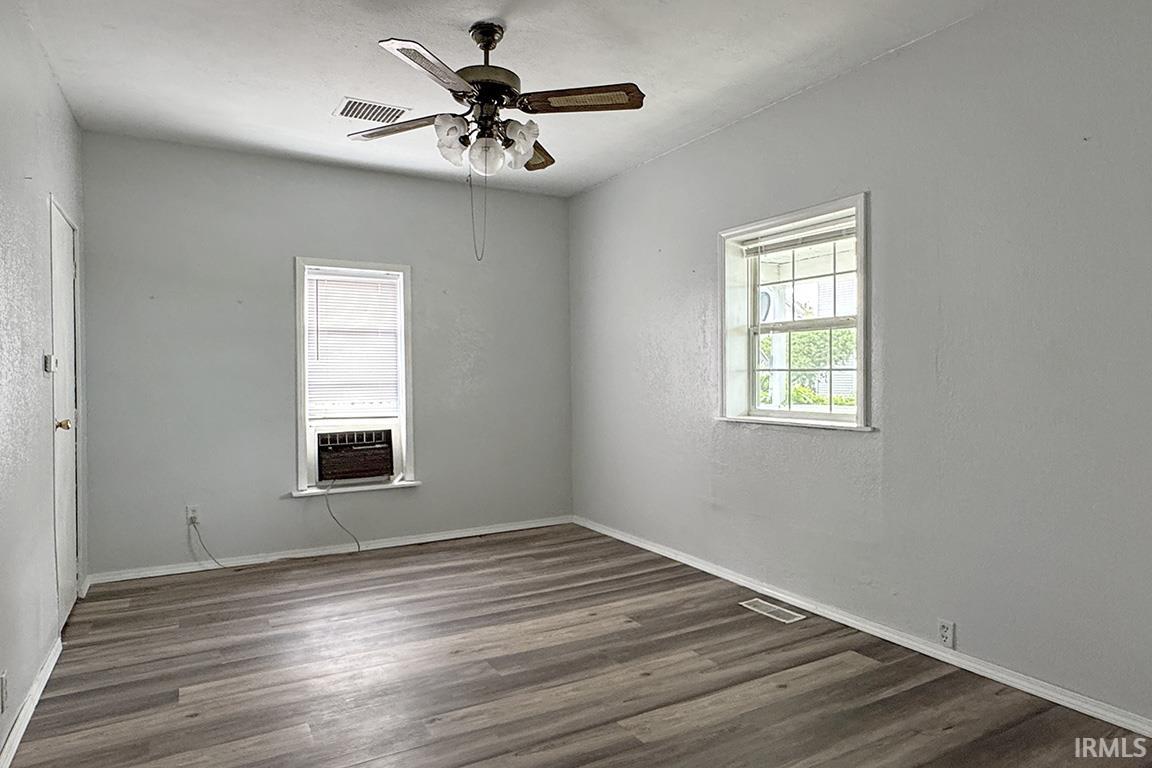 Neutral wall finishes, wood-finish flooring, two large windows, a ceiling fan with integrated lighting, and white trim