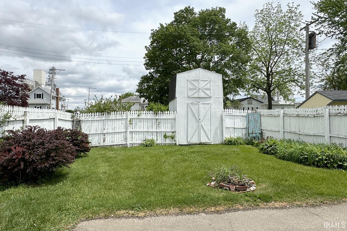 Rear yard featuring a white picket fence, a storage shed with double doors, and established perimeter landscaping