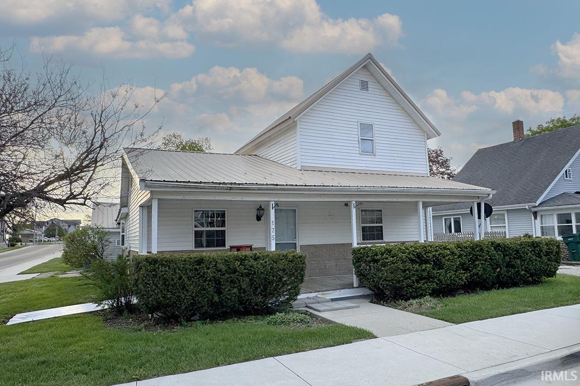 White siding residence featuring a metal roof, full-width covered porch, and mature front landscaping