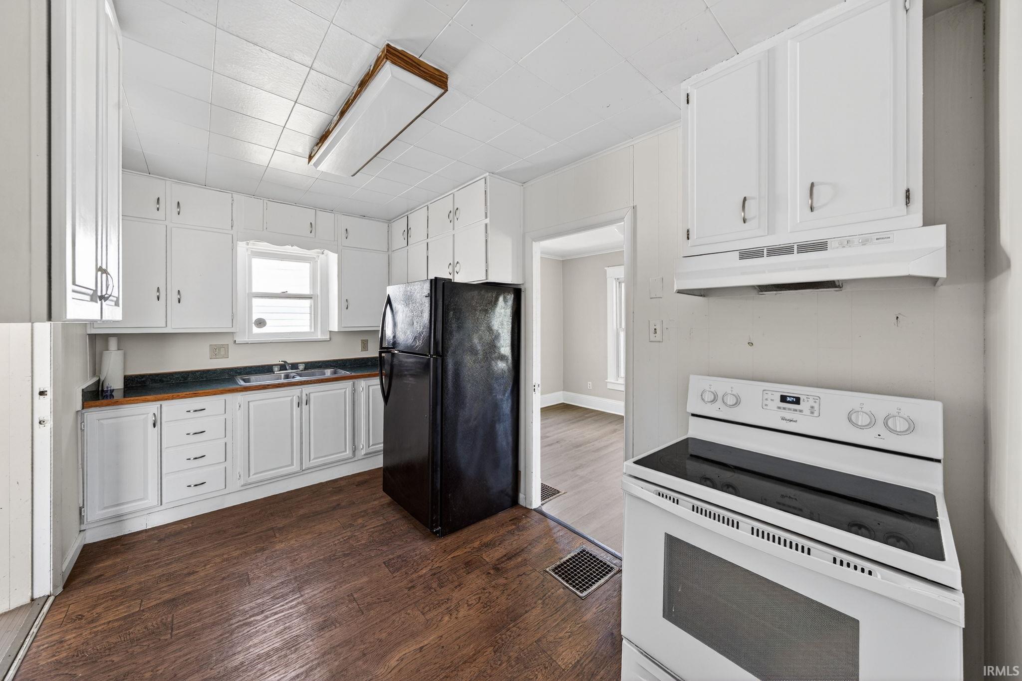 Bright kitchen with extensive white cabinetry, vinyl plank flooring, and a window above the sink