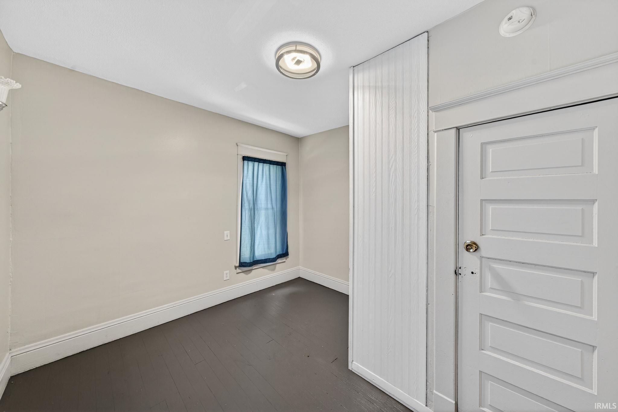 featuring a white paneled door, dark wood-finish flooring, and a flush-mount ceiling light fixture