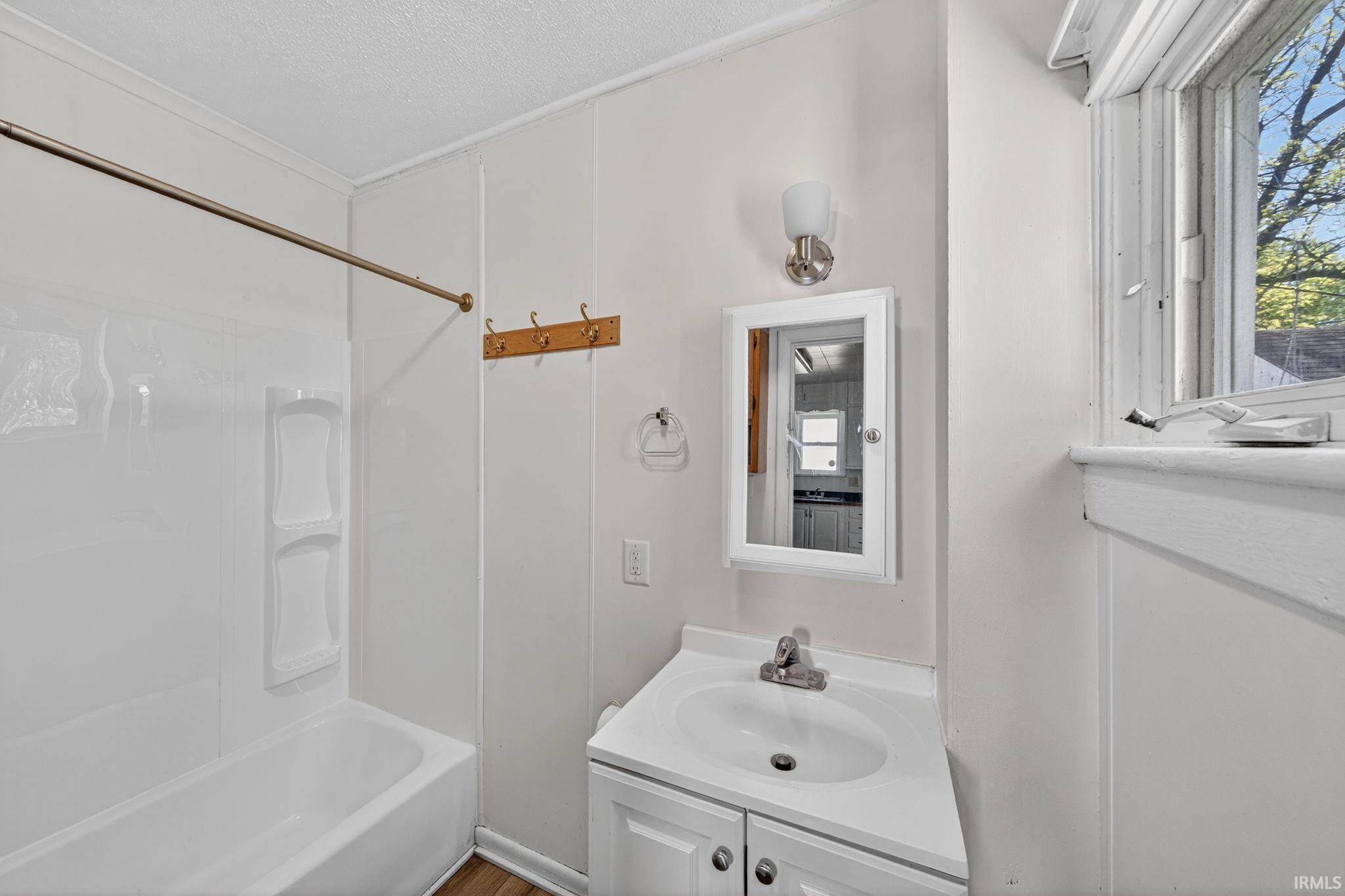 Full bathroom featuring a single vanity, a tub/shower combination with a shower curtain rod, a medicine cabinet, a wall-mounted light fixture, and a window