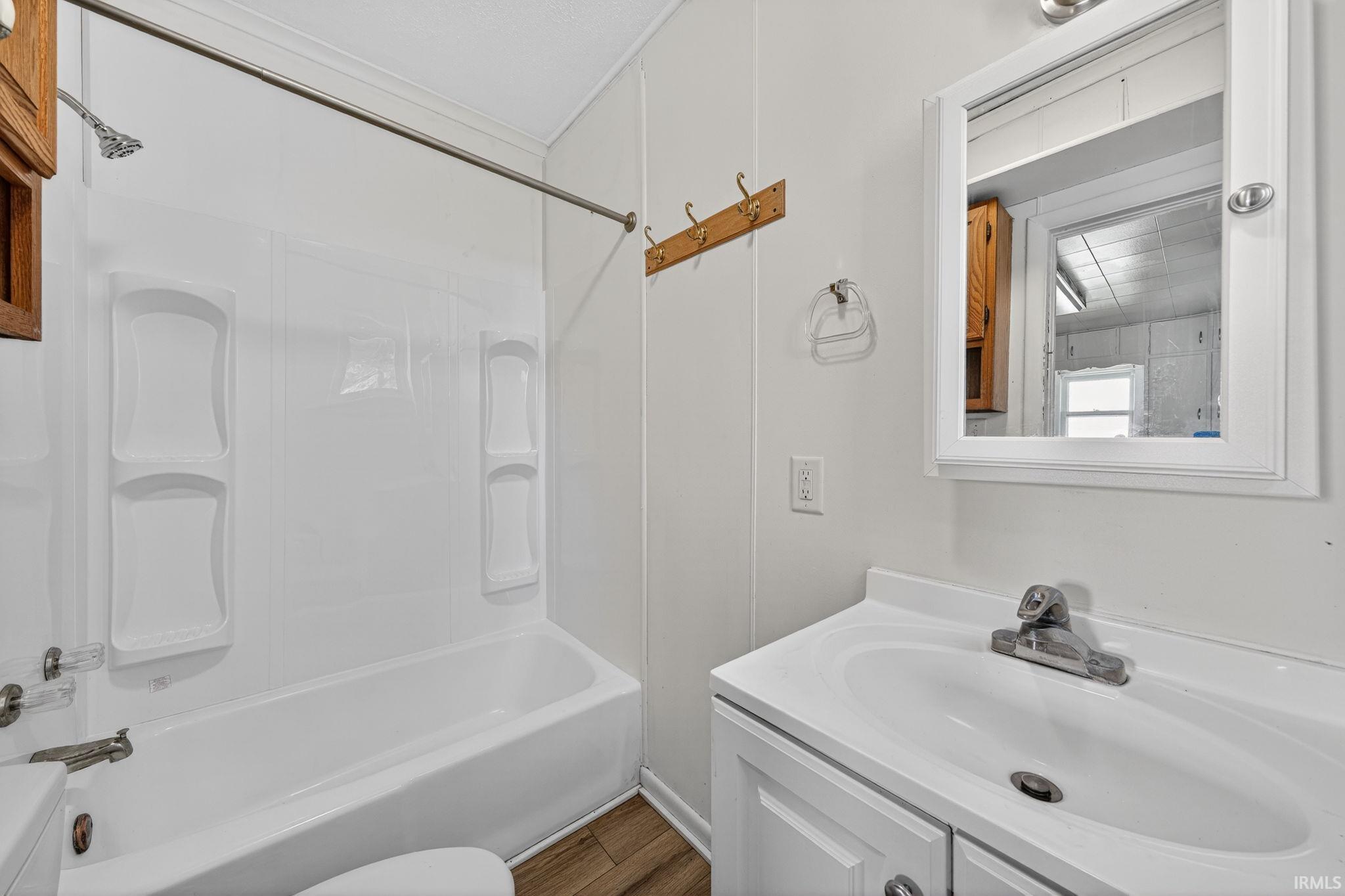 Bathroom featuring a white vanity with a single basin sink, a wall-mounted medicine cabinet, a full-size bathtub with white surround, and wood-finish flooring