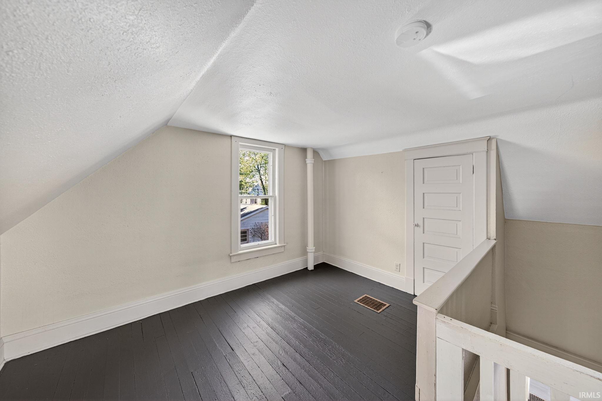 Loft space featuring dark wood-finish flooring, a single window, and sloped ceilings