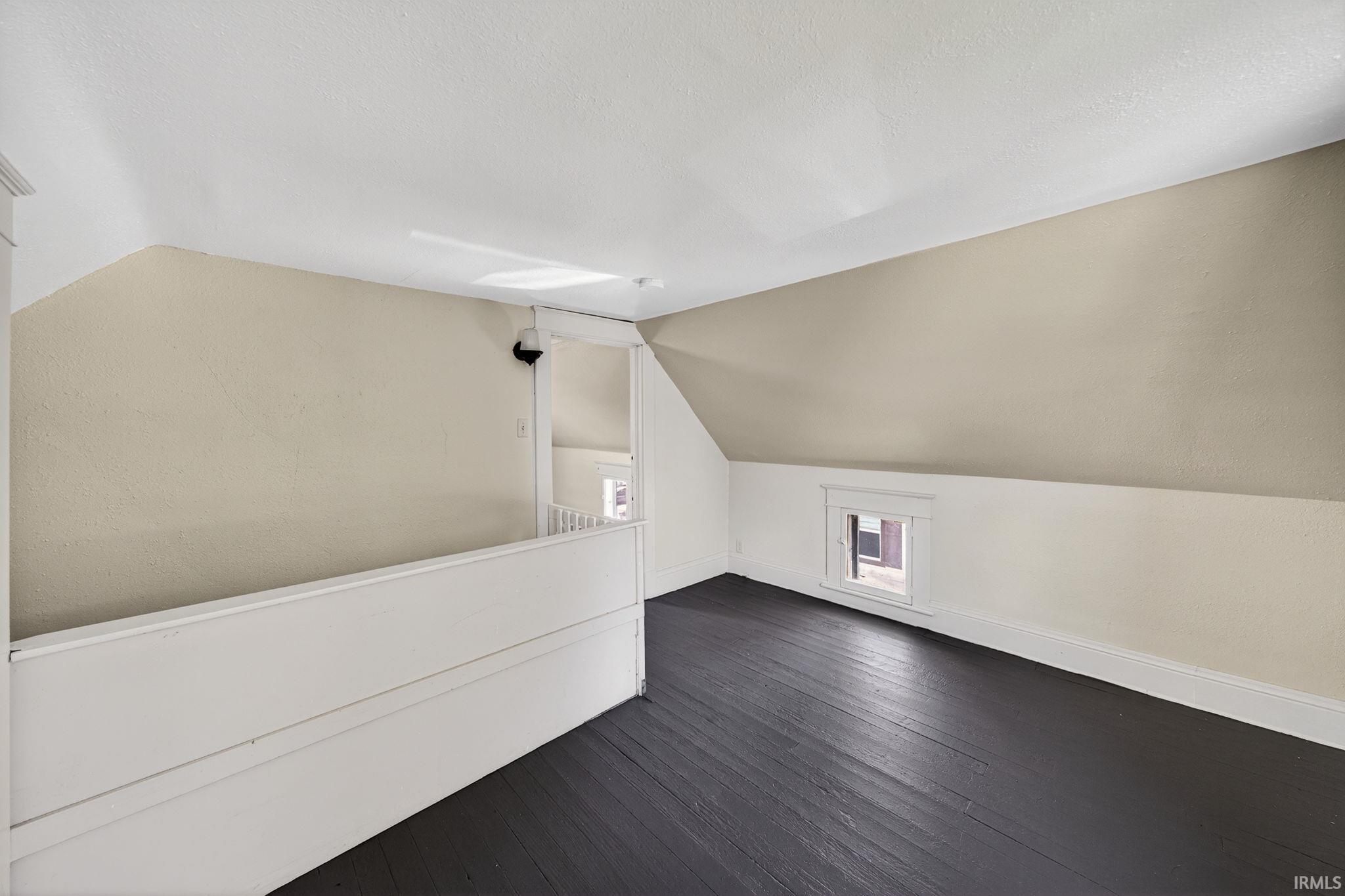 Loft featuring dark-stained wood-finish flooring, sloped ceilings, and a dormer window