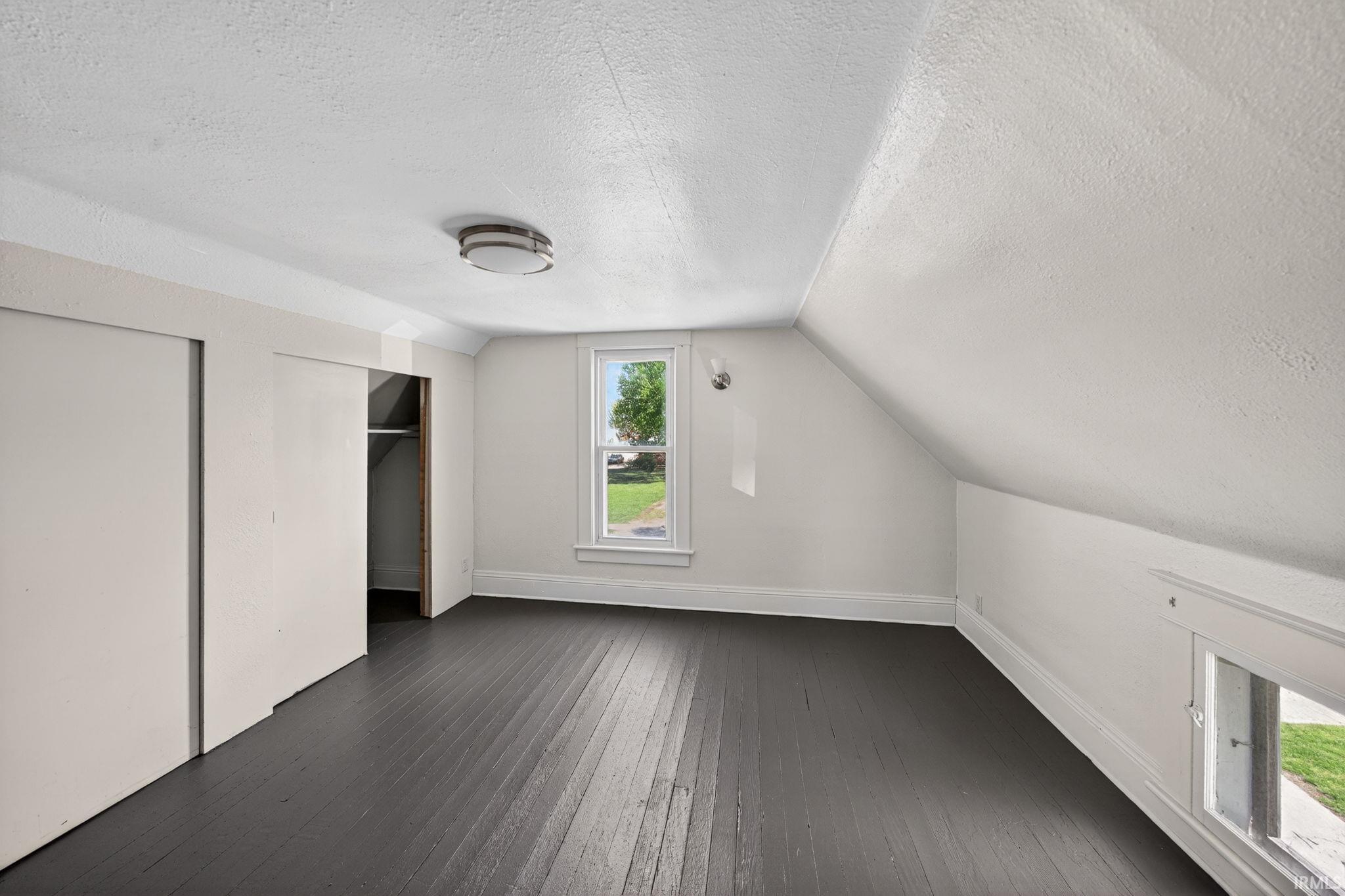 Upper level bedroom featuring dark wood-finish flooring, white walls, and a sloped ceiling