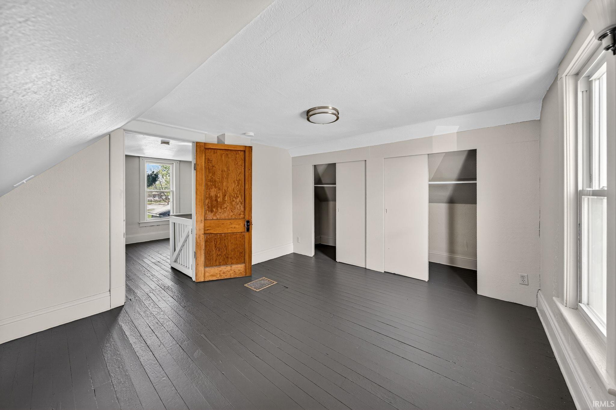 Spacious room featuring painted wood flooring, sloped ceilings, and built-in sliding closet doors