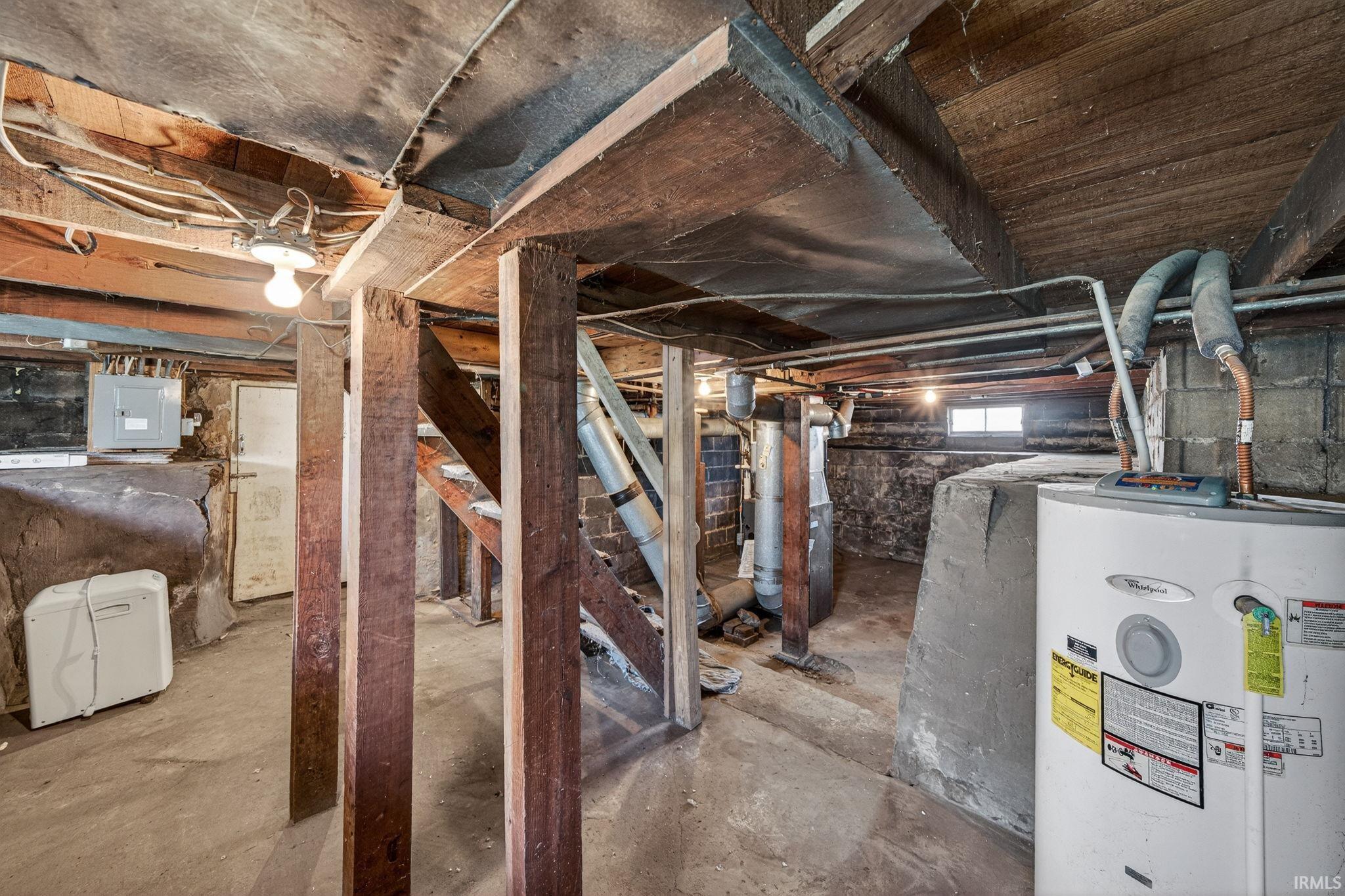Basement space featuring exposed wood beam ceiling, concrete foundation walls, and a visible water heater unit