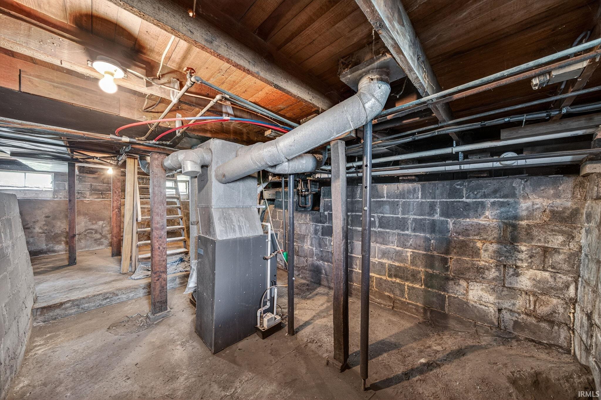 Unfinished basement featuring exposed wood ceiling joists, a furnace unit with ductwork, concrete block walls, and visible utility lines