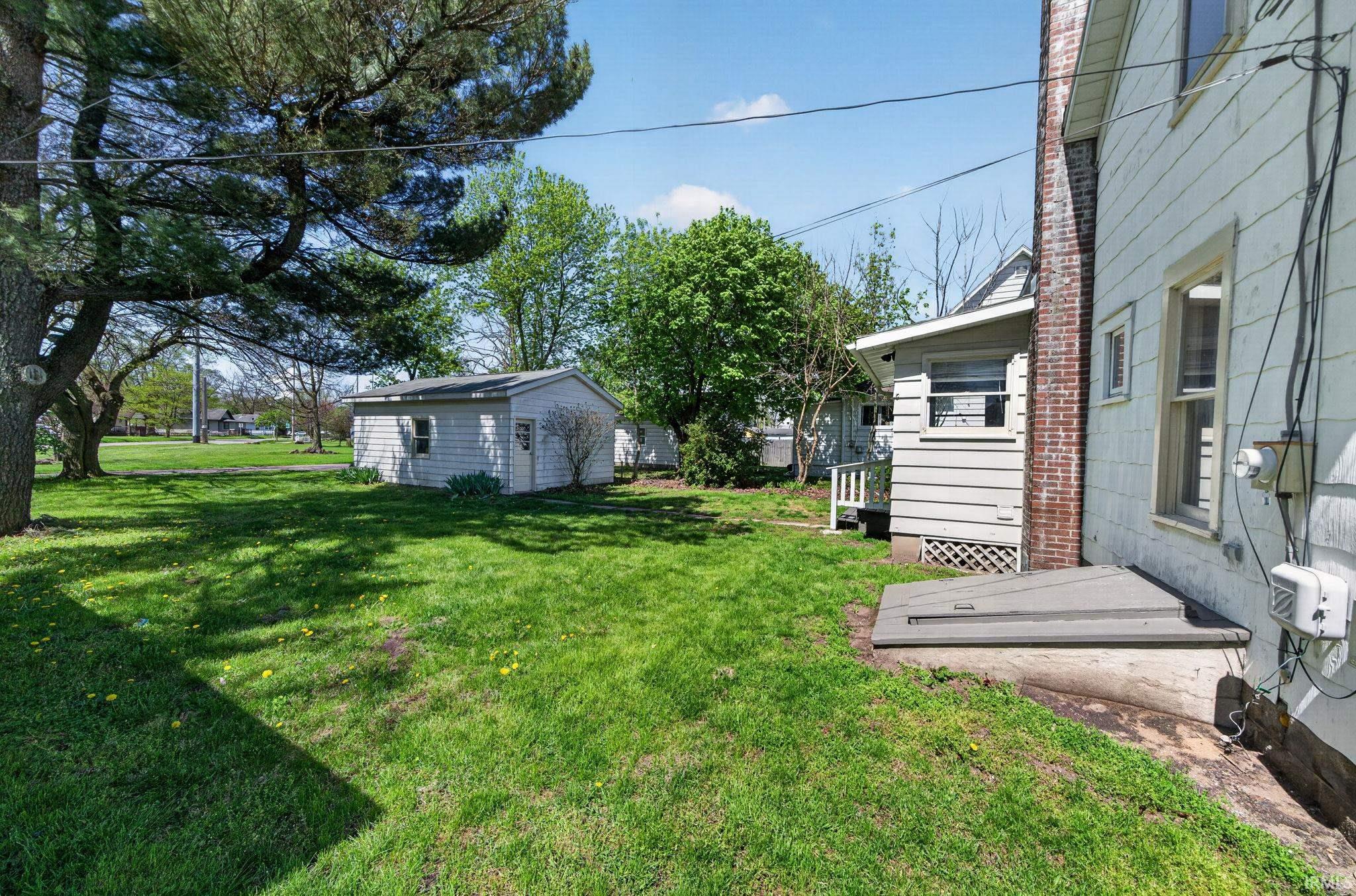 Expansive lawn featuring mature trees, a detached storage shed, and a property exterior with white siding