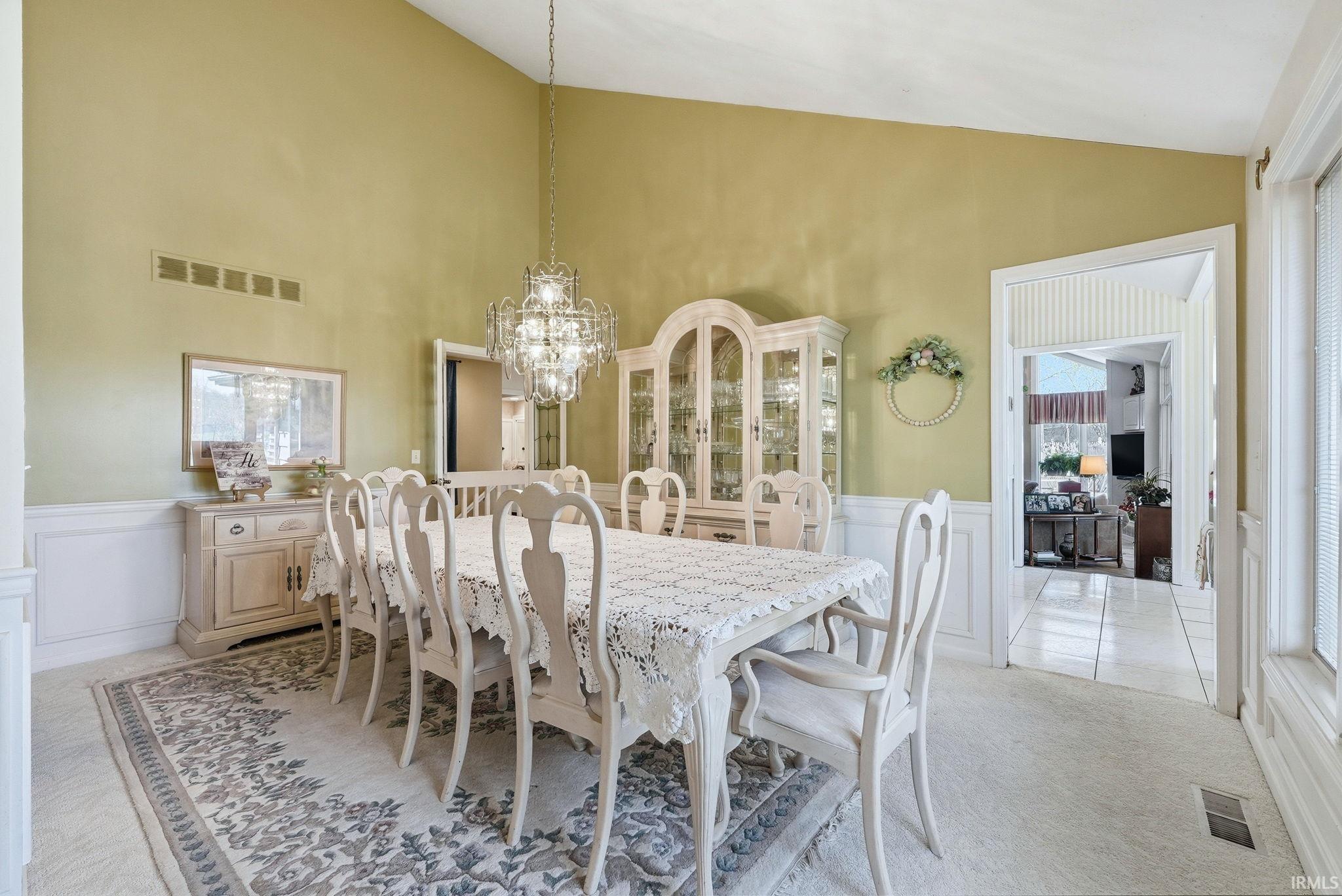 Dining area with lofted ceiling, a wainscoted wall, a decorative wall, light carpet, and suspended lighting