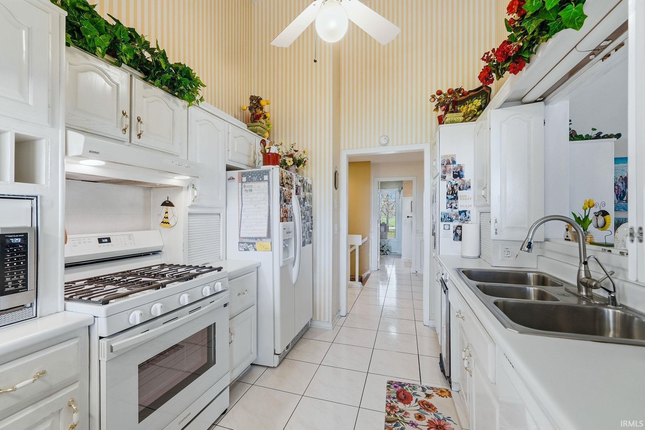 Kitchen featuring white appliances, white cabinetry, light countertops, light tile patterned flooring, and a ceiling fan