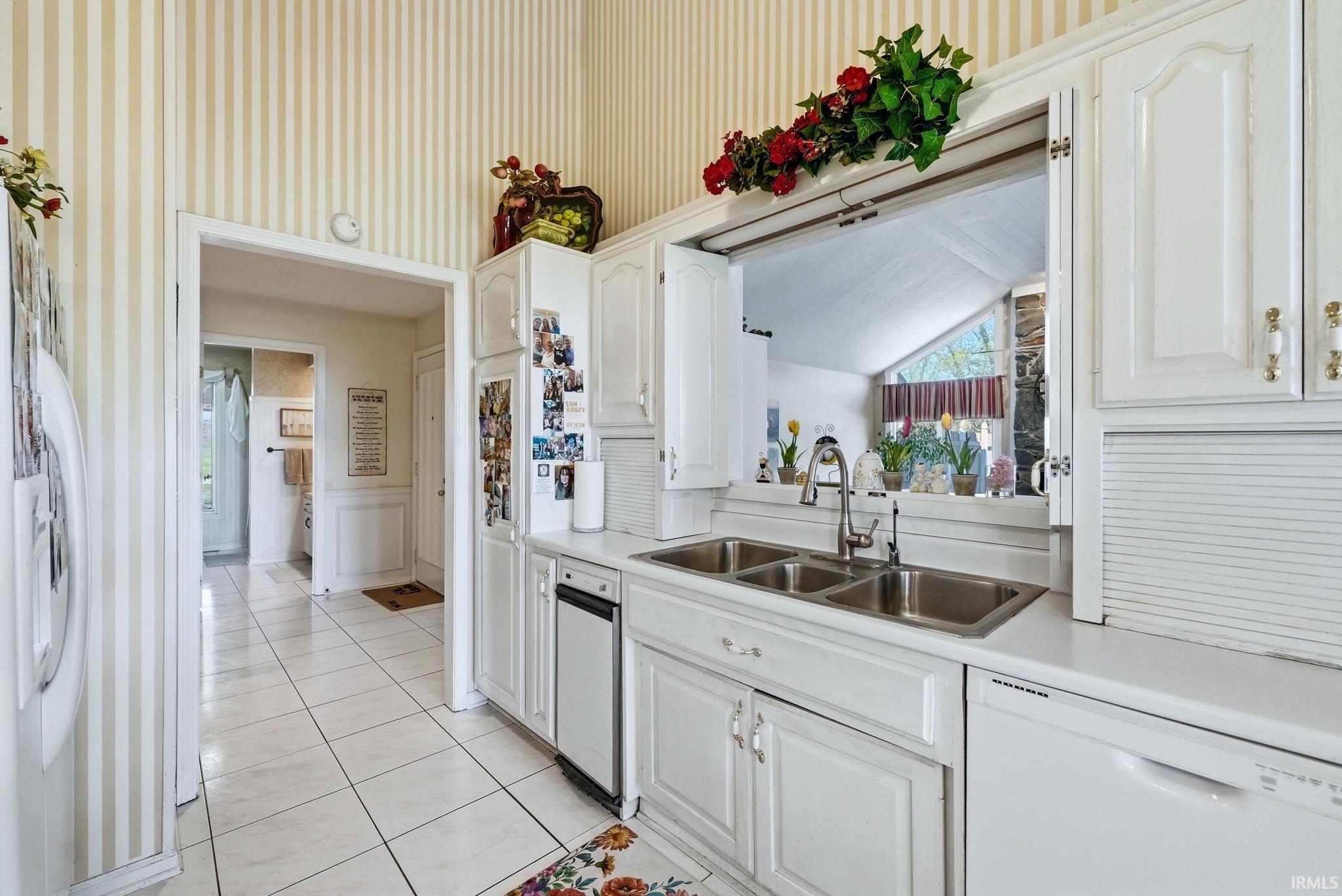 Kitchen with wallpapered walls, dishwasher, light countertops, wainscoting, and white cabinetry